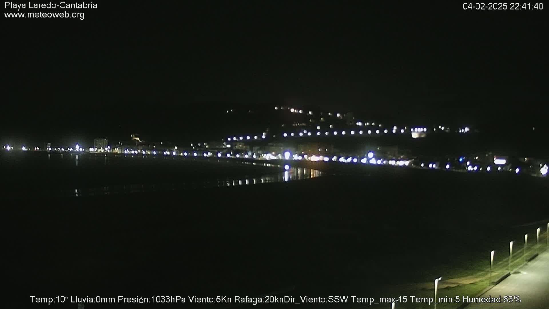A nighttime view of a dark beach with a line of lights illuminating buildings on a hill in the distance.