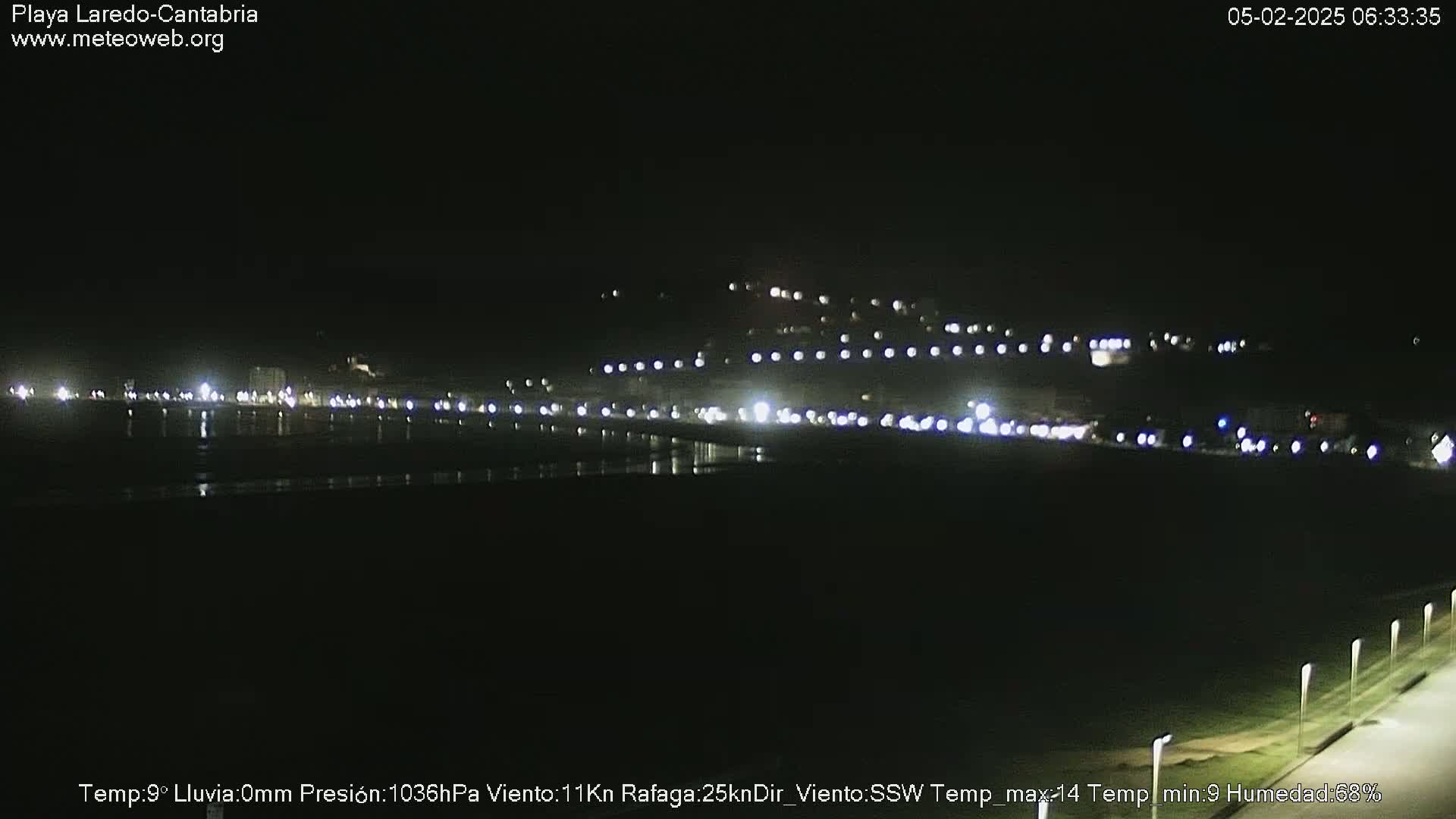 A nighttime view of a dark beach with a line of lights from buildings and vehicles in the distance.