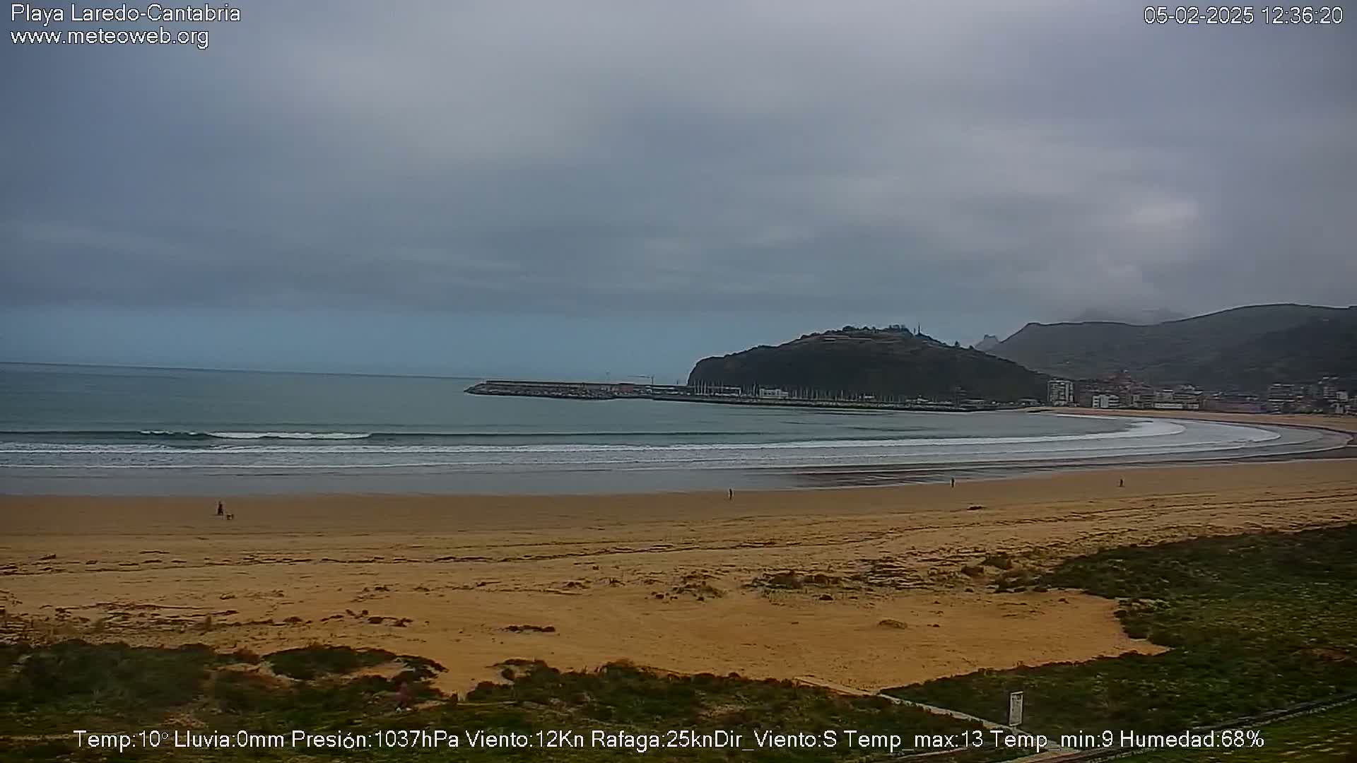 A wide sandy beach curves around a calm bay under an overcast sky.
