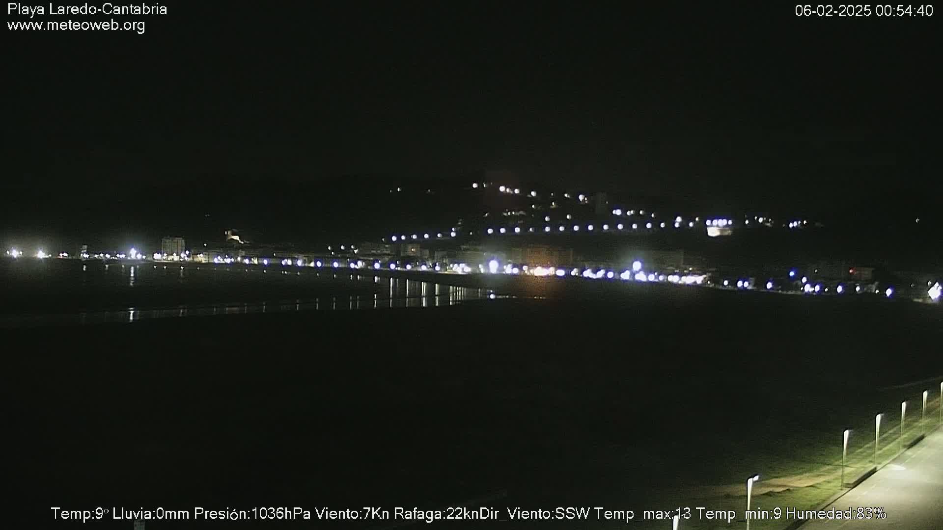 A nighttime view of a dark beach and dimly lit town along a coastline.
