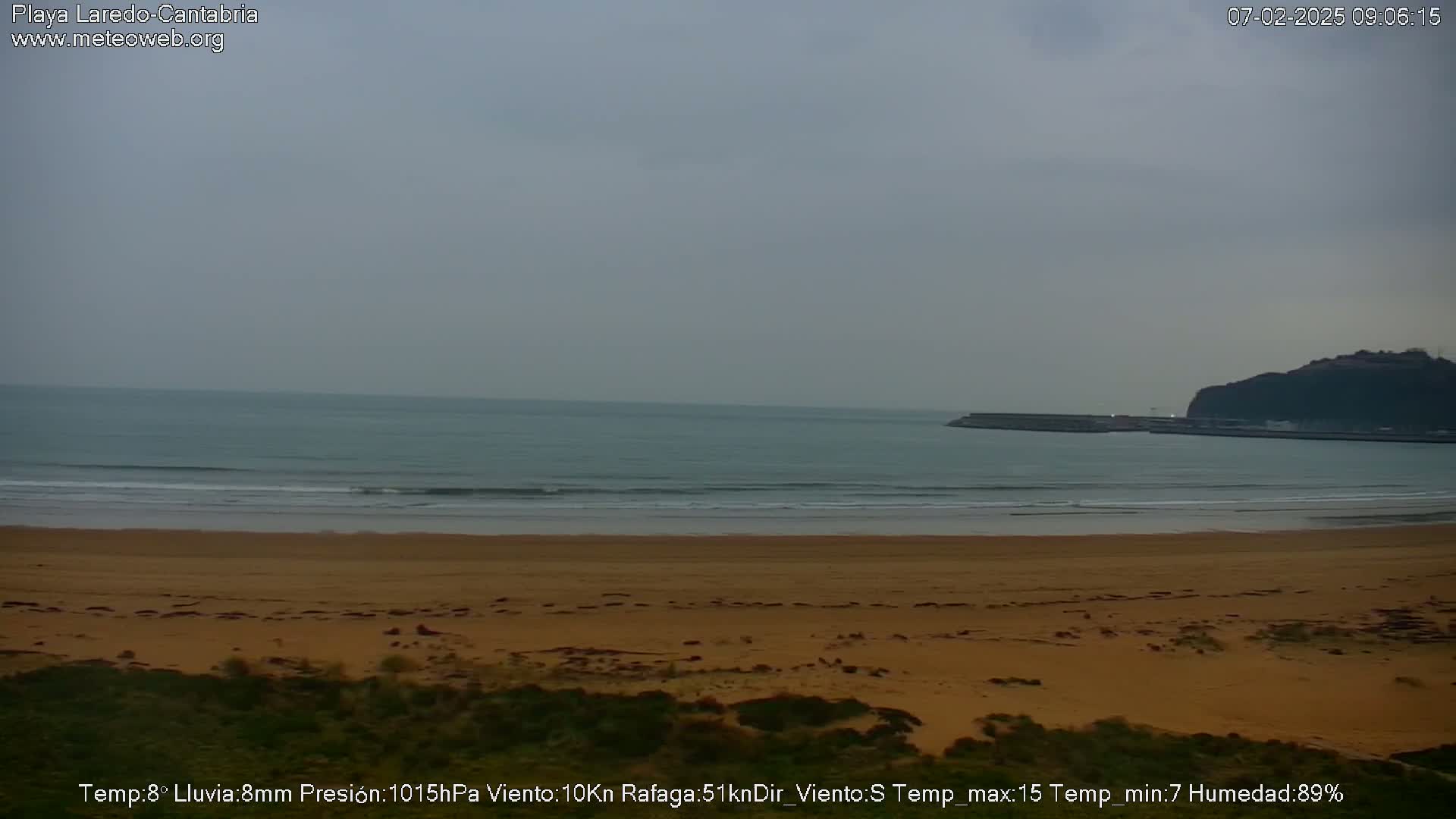 A sandy beach stretches out to a calm, grey ocean under an overcast sky.