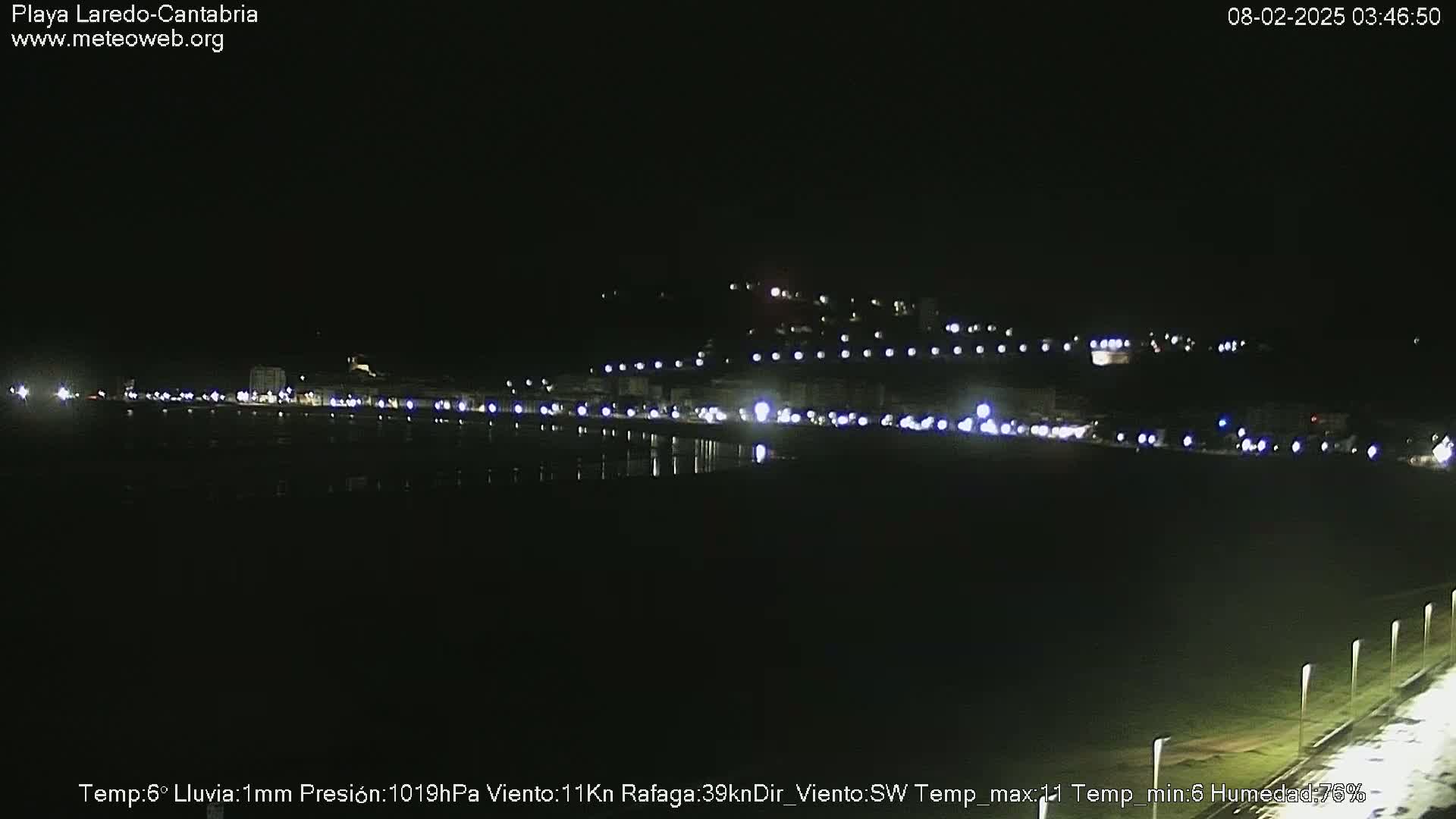 A nighttime view of a dimly lit coastal town with a calm, dark body of water reflecting the lights.