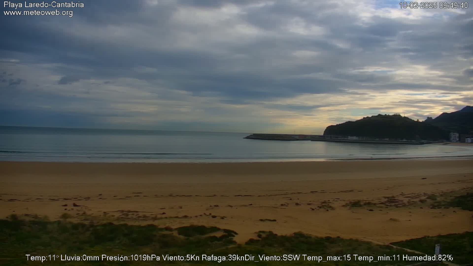 A sandy beach stretches out to a calm sea under a mostly cloudy sky.