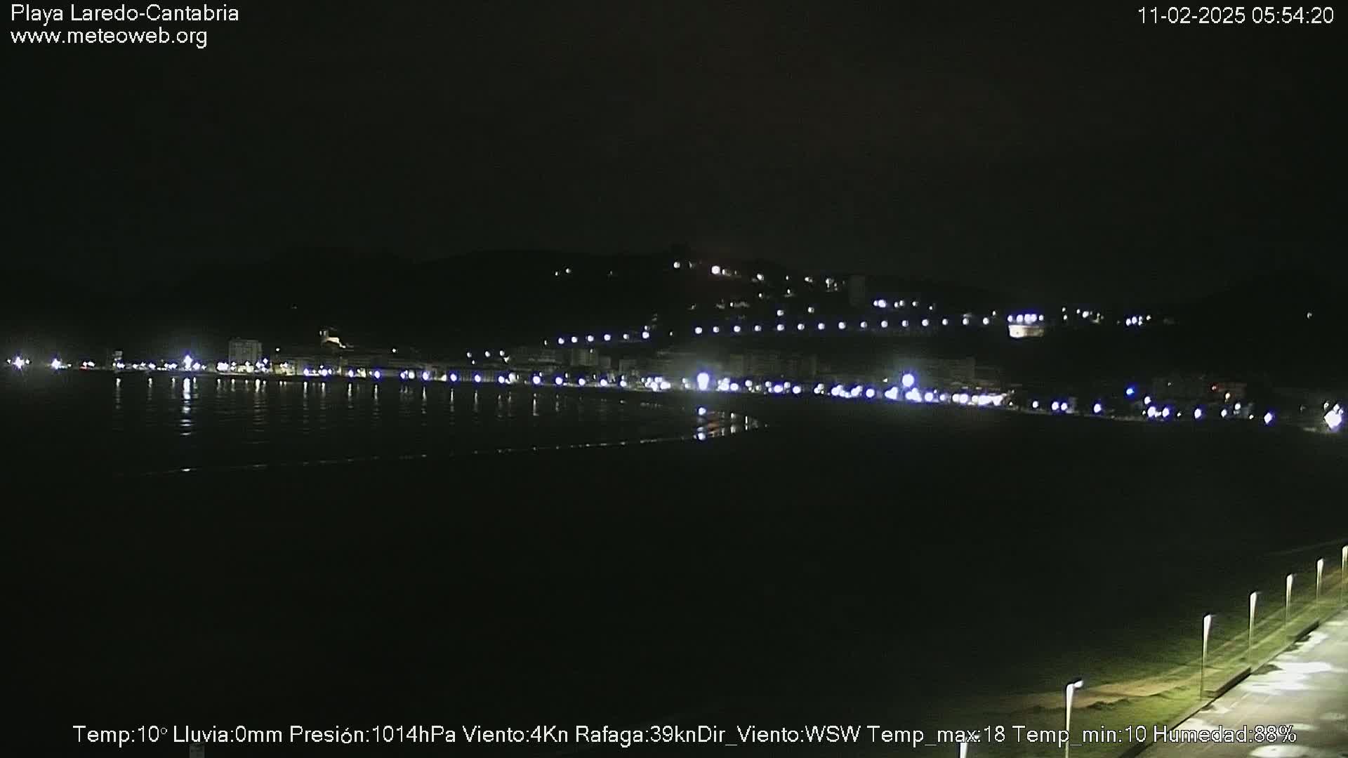 A nighttime view of a dimly lit coastal town and beach, with a calm, dark sea.