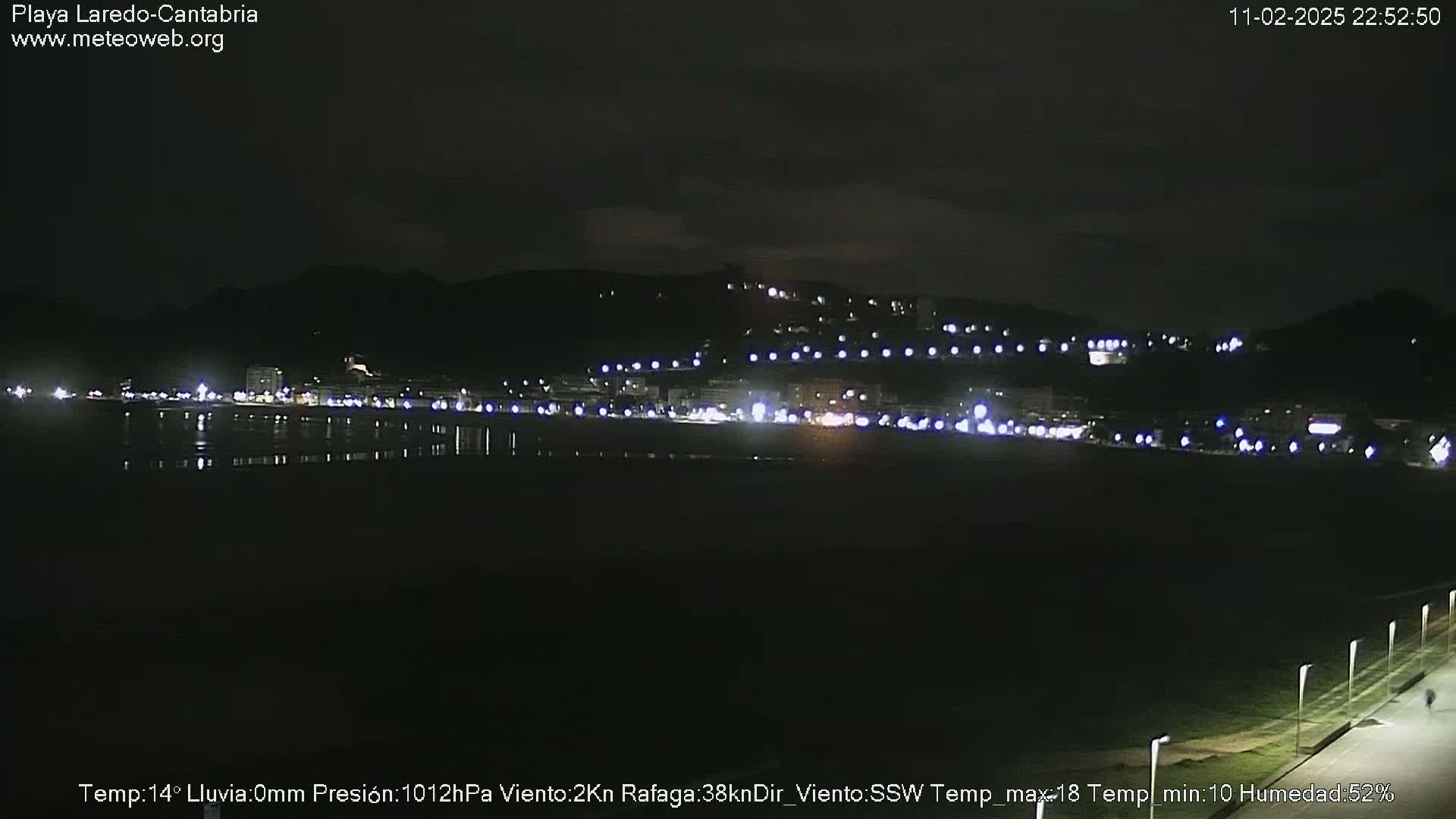 A nighttime view of a town's lights along a dark shoreline, under a clear sky.
