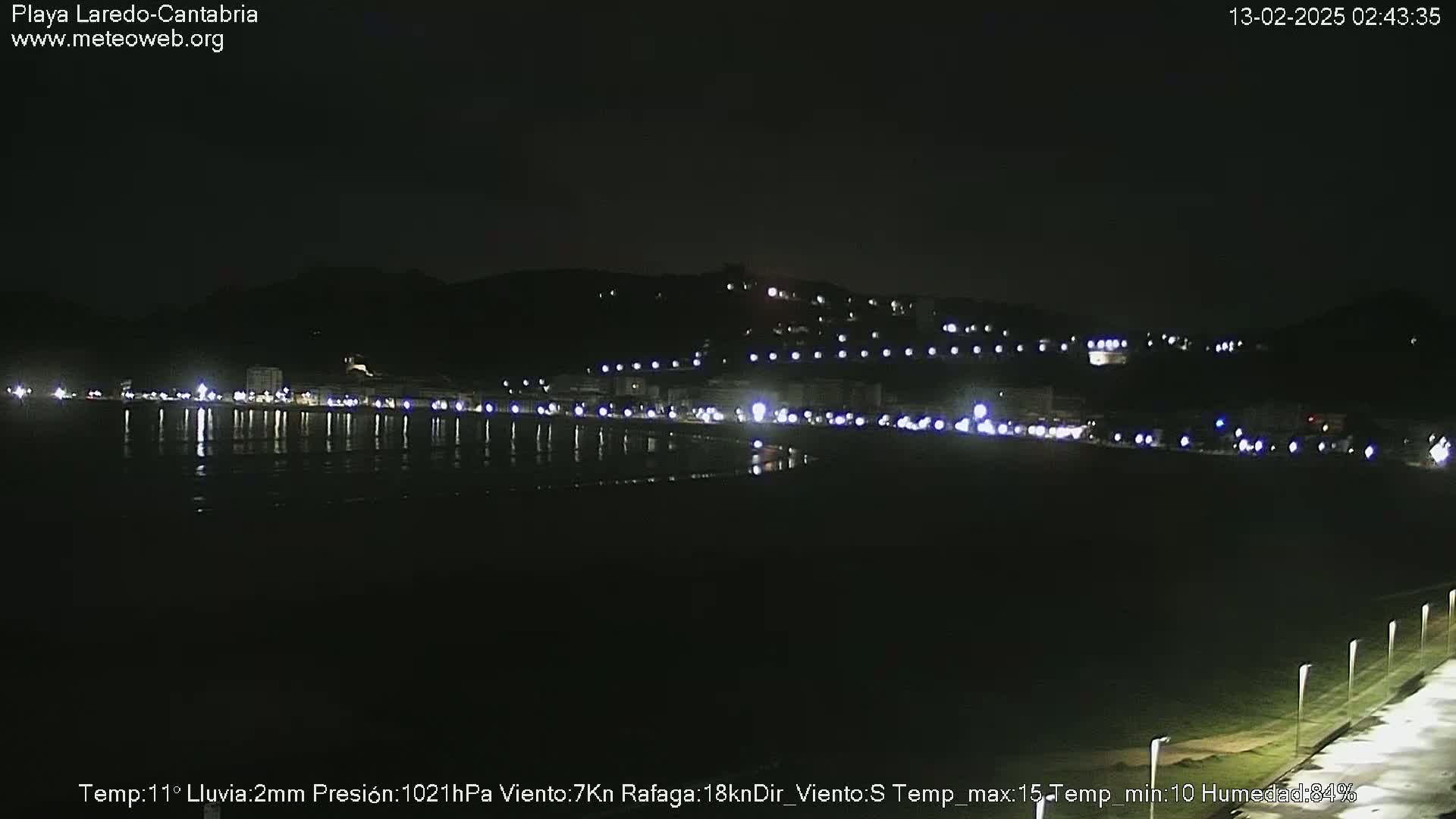 A nighttime view of a dimly lit beach town and coastline, with light rain.