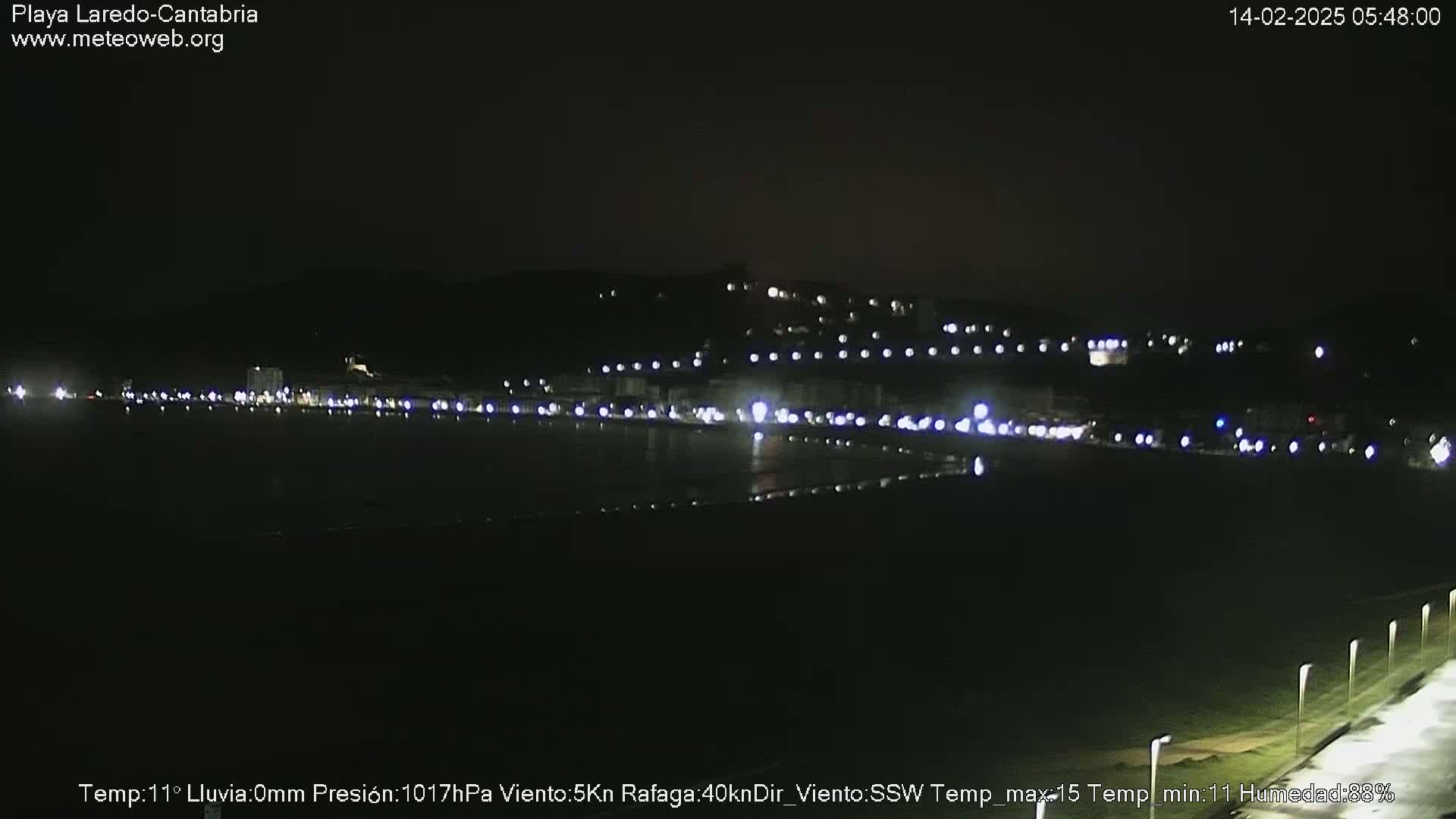 A nighttime view of a coastal town with its lights illuminating the dark beach and water under a clear sky.