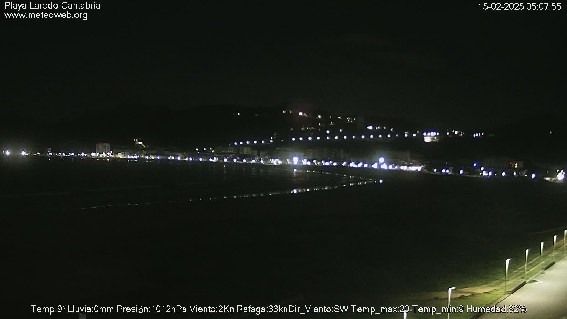 A nighttime view of a dark, flat coastal area with a line of lights on the horizon.