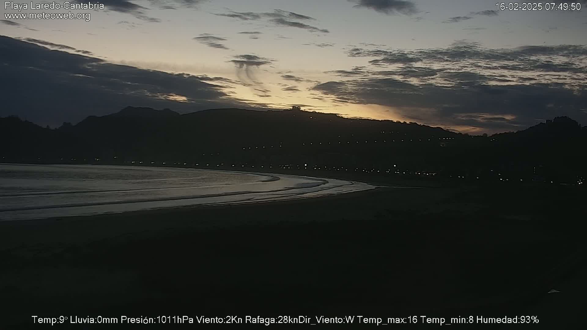 A dark beach at sunset under a mostly cloudy sky.