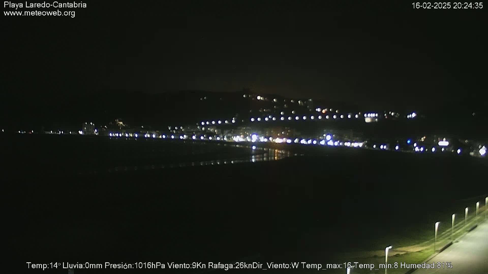 A nighttime long shot of a dimly lit coastal town and beach under a clear, dark sky.