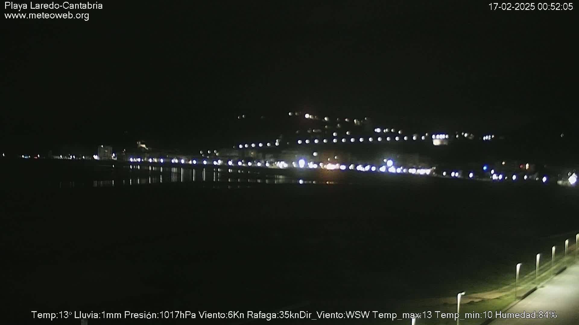 A nighttime view of a town's lights across a dark body of water under a slightly rainy sky.