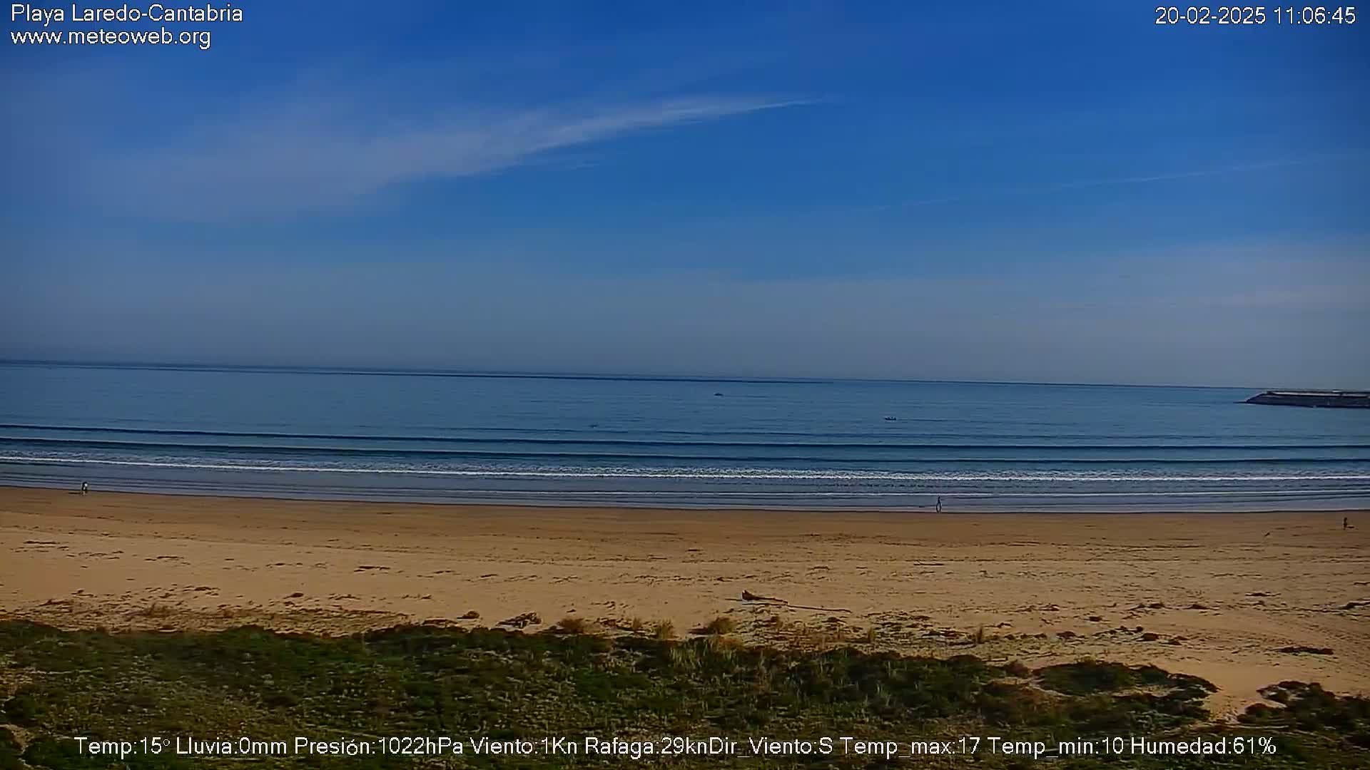 A sandy beach with gentle waves under a clear blue sky meets a calm ocean.
