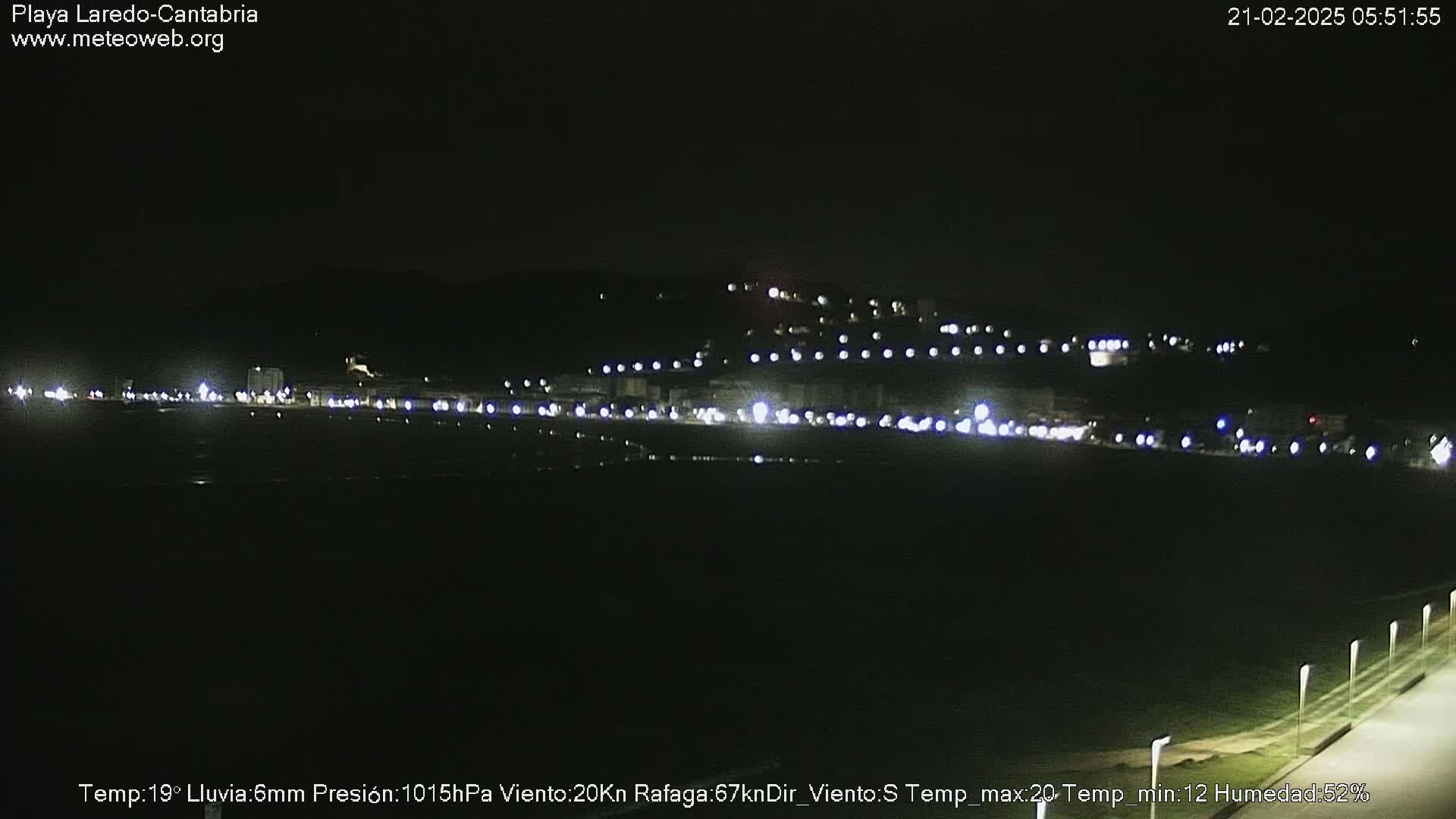 A nighttime view of a dimly lit coastal town with a dark sky and light rain.