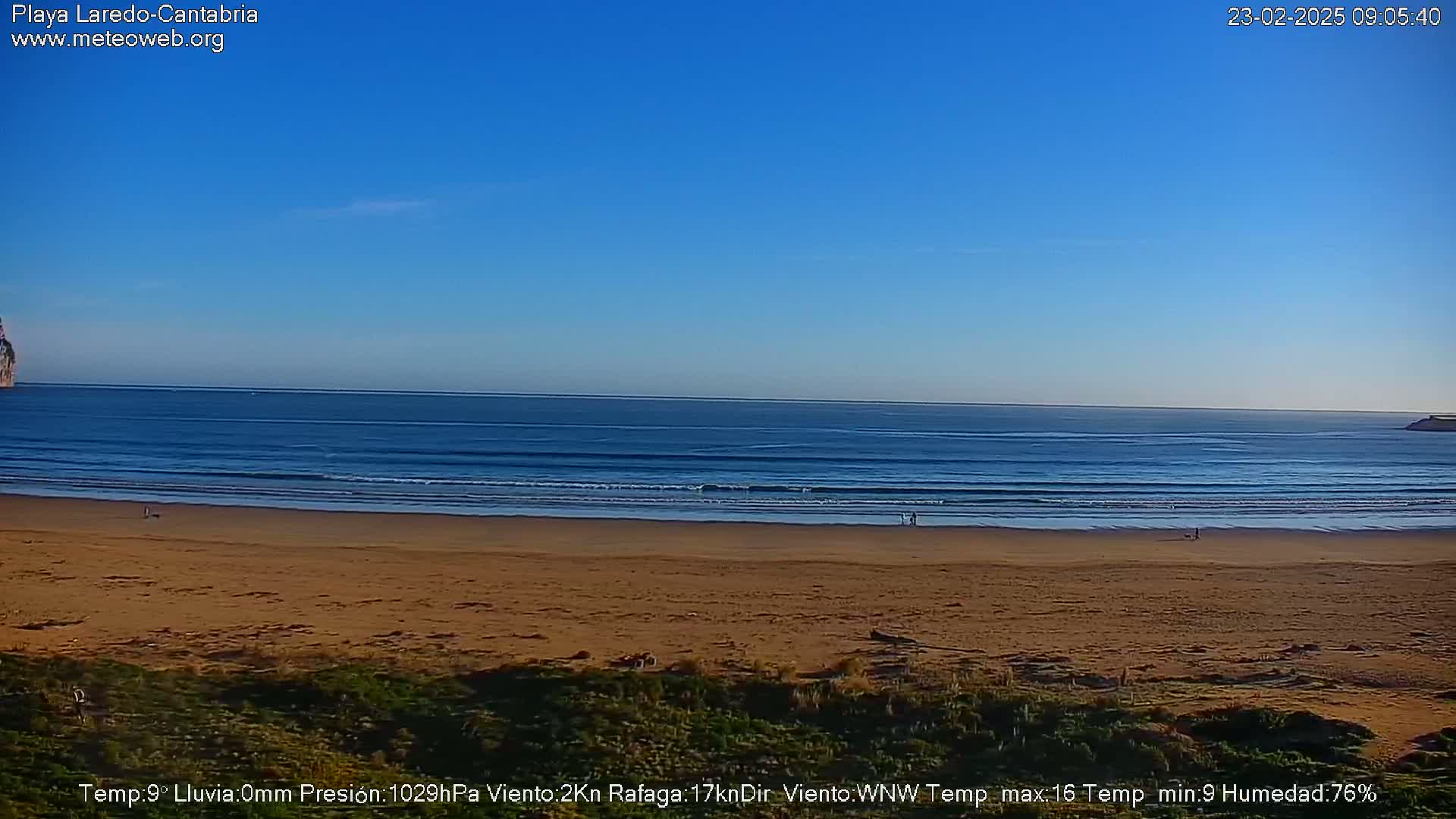 A sandy beach stretches to a calm ocean under a clear blue sky.
