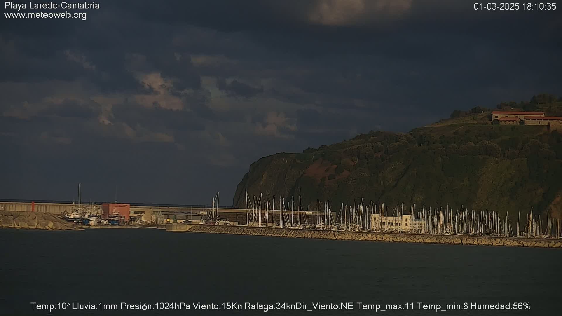 A harbor filled with numerous boats is situated beneath a dark, cloudy sky.