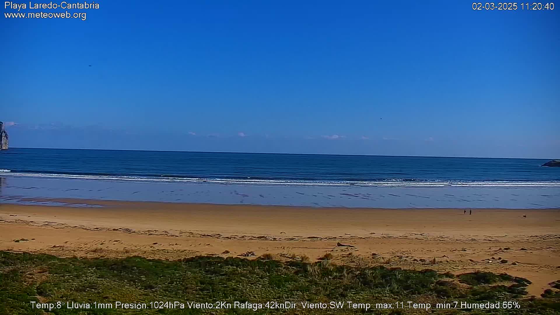 A sandy beach stretches to a calm ocean under a clear blue sky.