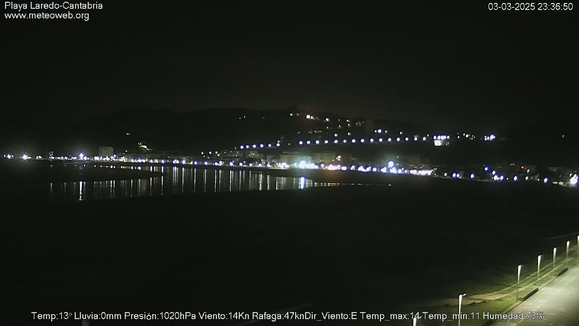 A nighttime view of a coastal town with lights reflecting on the water under a clear, dark sky.