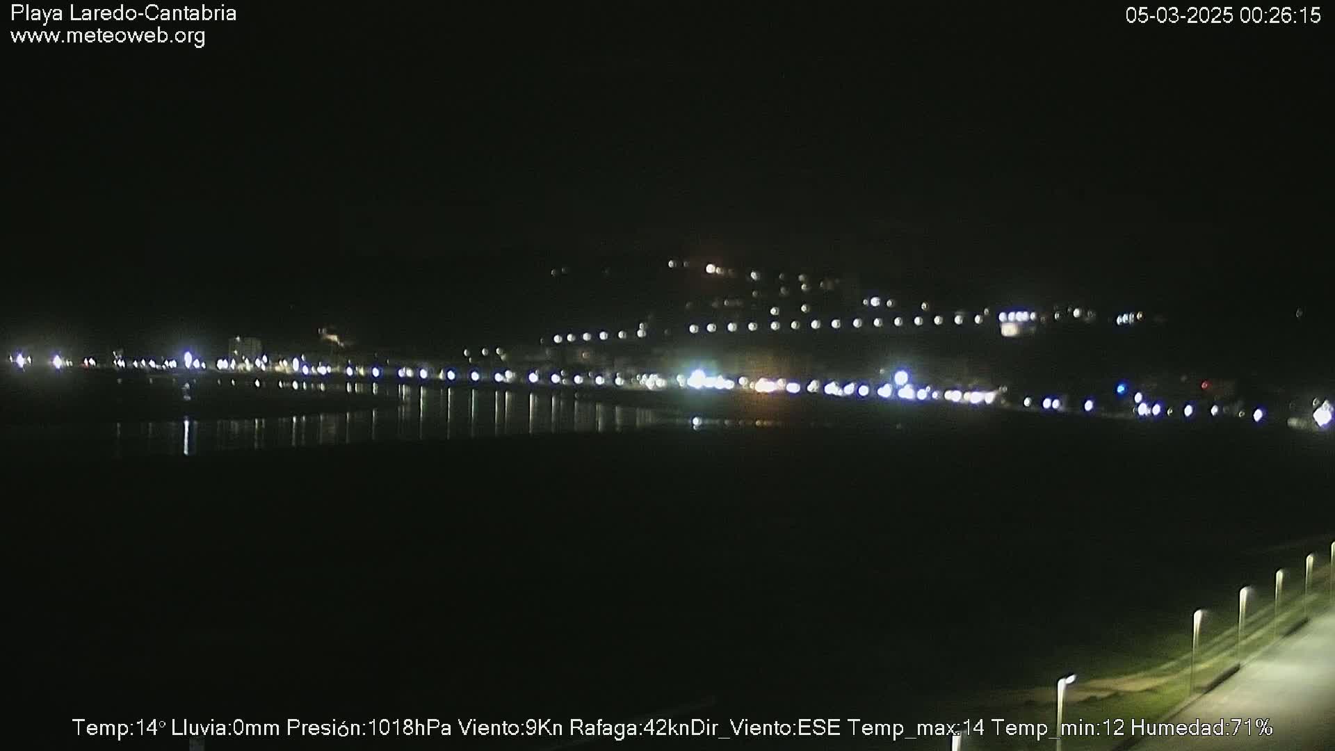 A nighttime view of a dark, calm body of water reflecting the lights of a distant town.
