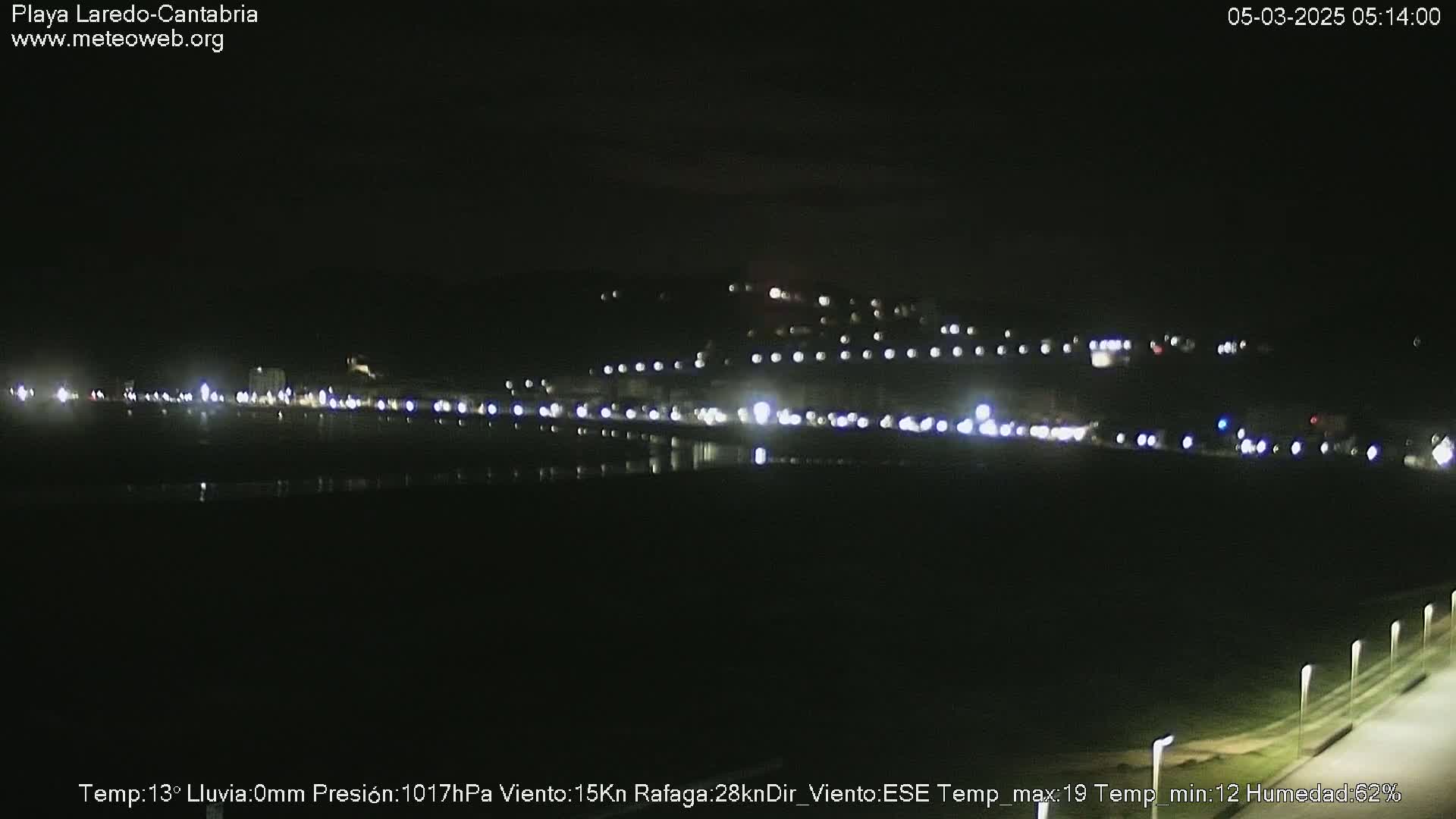 A nighttime view of a coastal town with its lights reflected on a dark body of water.