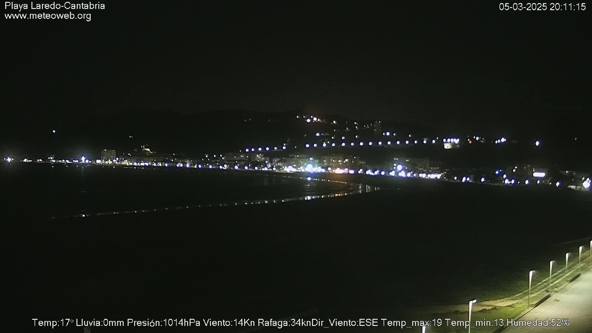 A nighttime view of a coastal town with its lights reflecting on dark water under a clear sky.