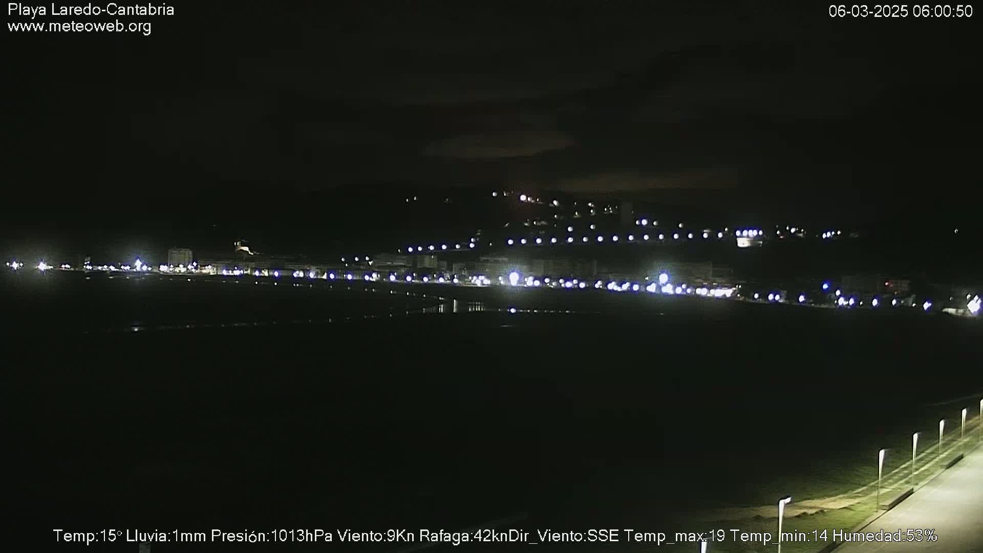A nighttime view of a dimly lit beach and town, with light rain.