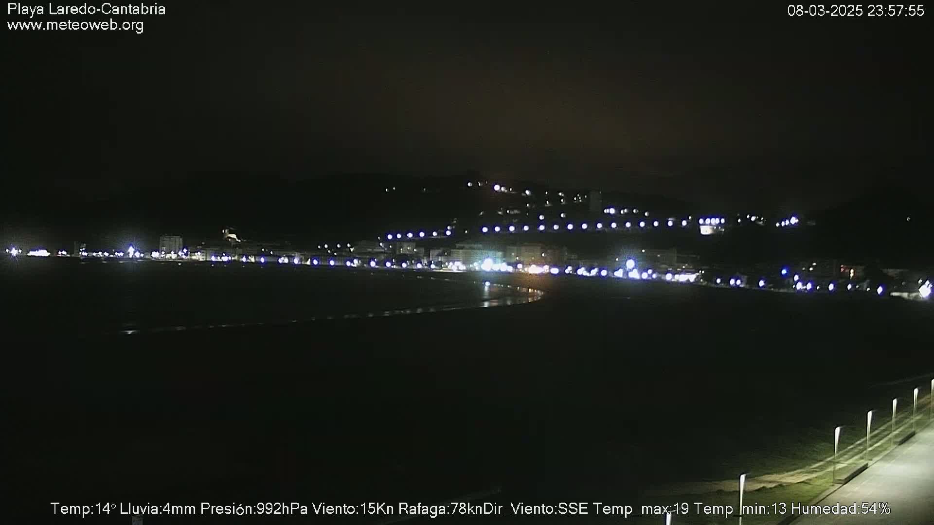 A nighttime view of a dimly lit beach and town, with rain and a strong wind blowing from the southeast.