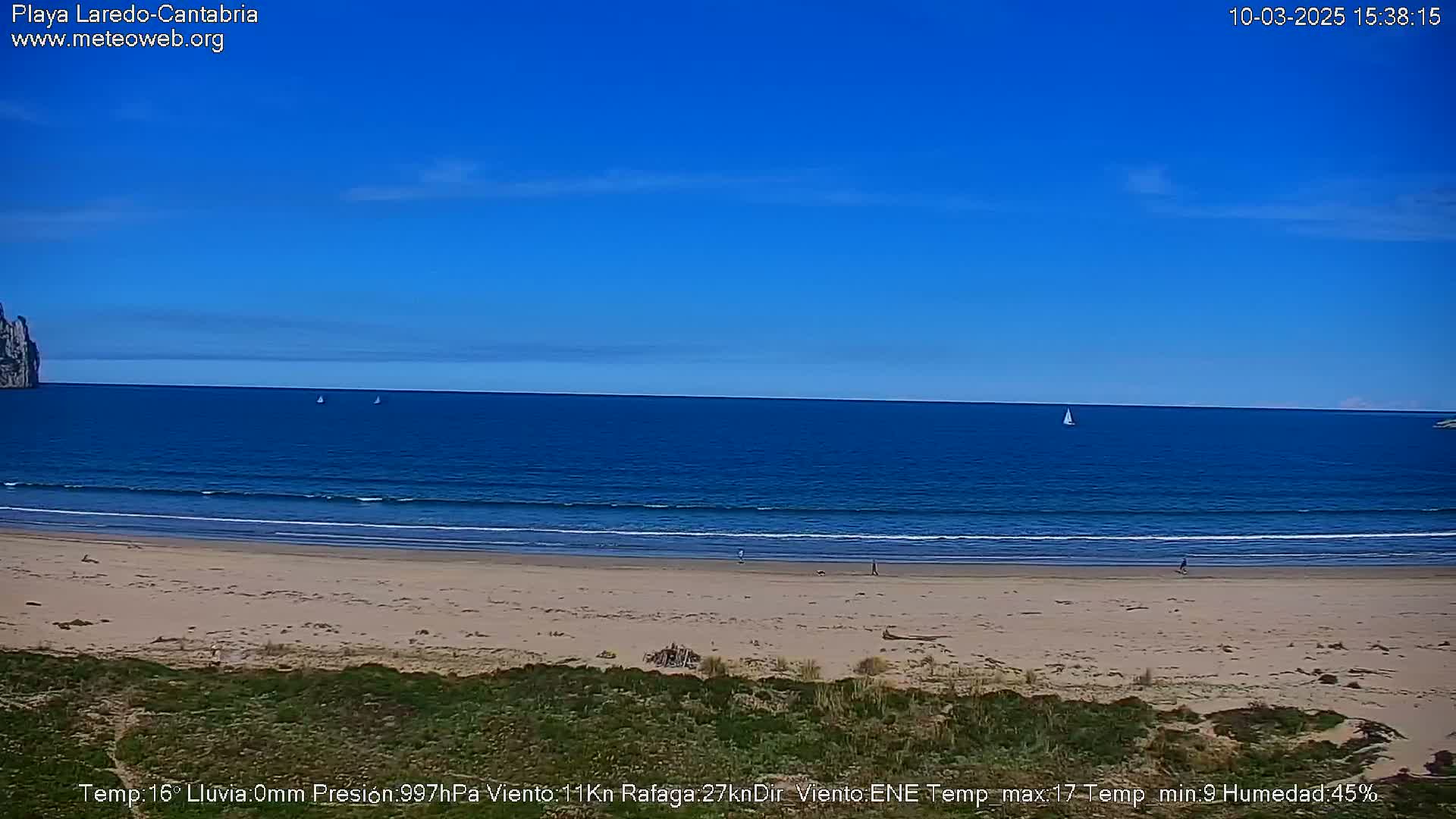 A sandy beach with a calm, blue ocean under a clear blue sky is shown.