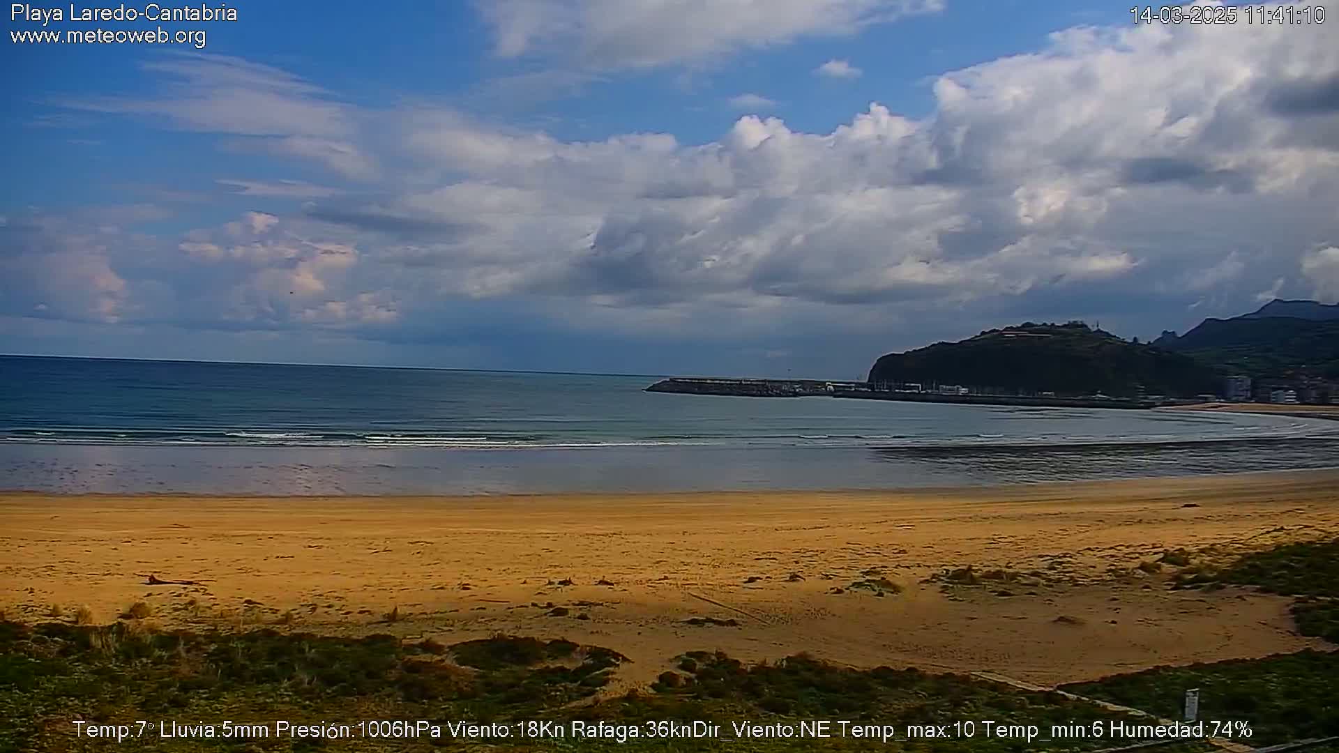 A sandy beach stretches to a calm ocean under a partly cloudy sky.
