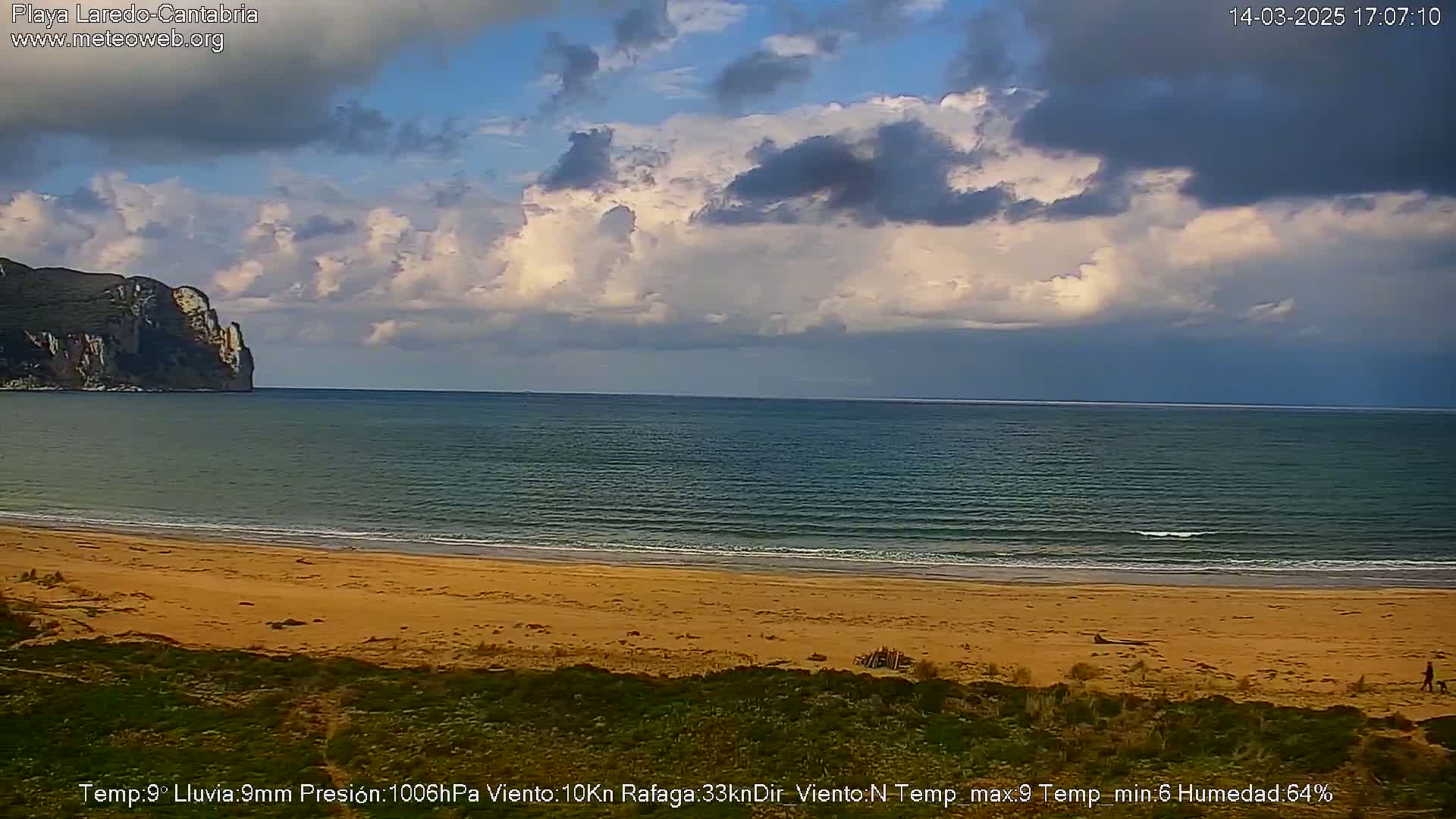 A sandy beach stretches to a calm sea under a partly cloudy sky.