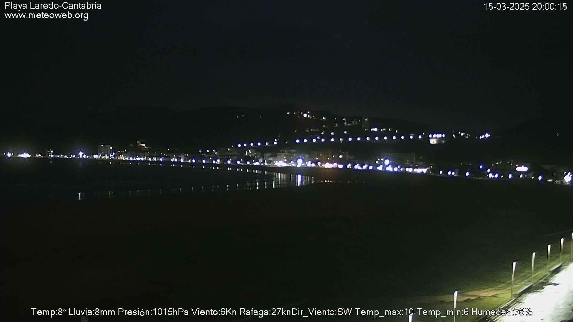A nighttime view of a city's lights along a dark beach under a clear sky.