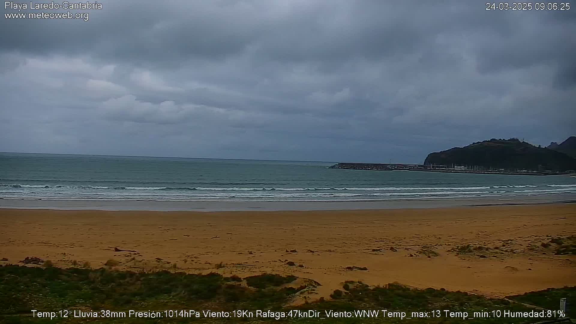 A sandy beach with gentle waves stretches to a calm ocean under a cloudy sky.