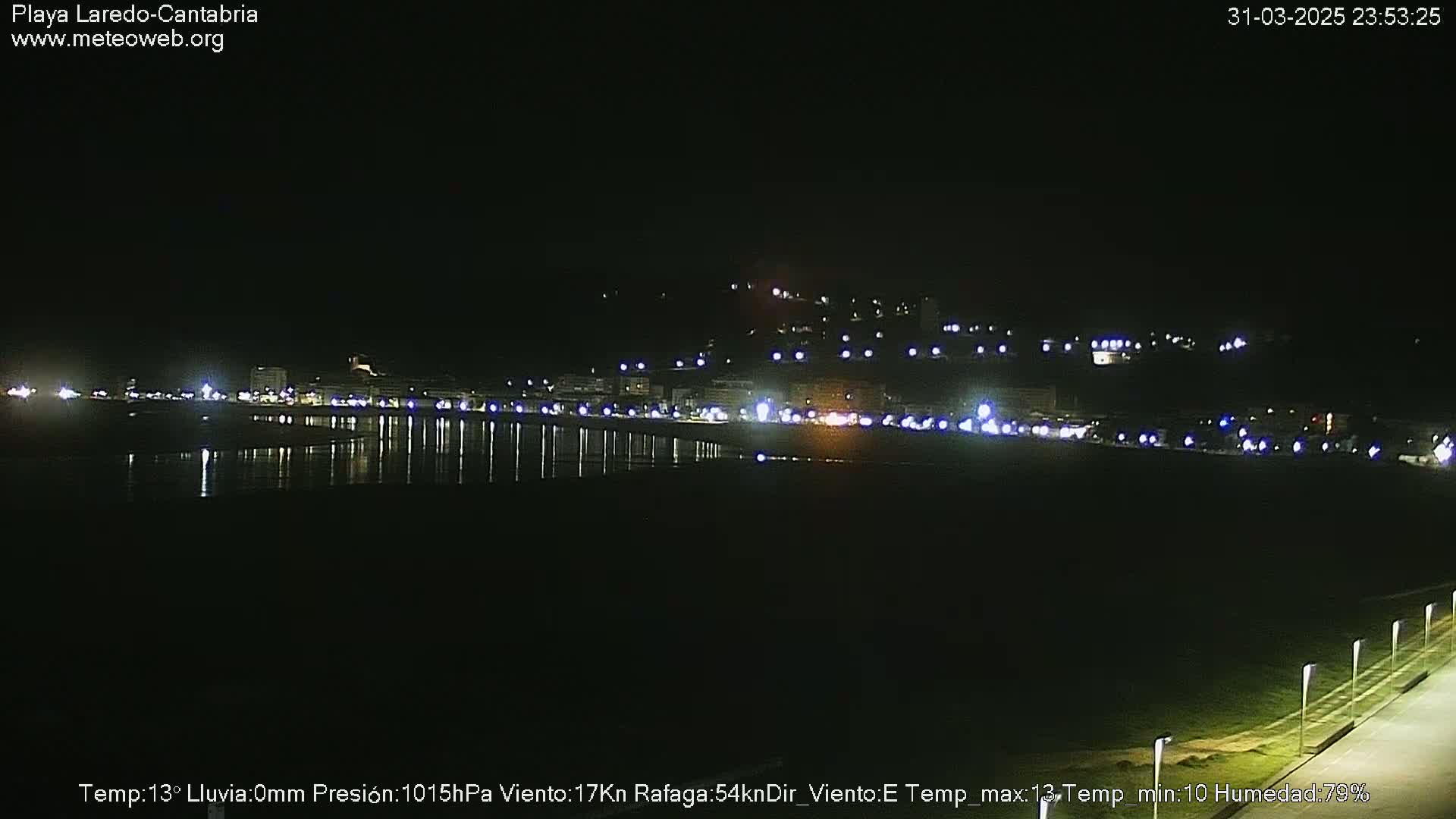 A nighttime view of a coastal town with its lights reflecting on a calm body of water.