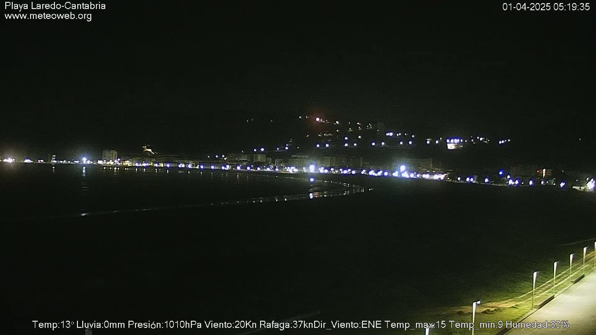 A nighttime view of a coastal town, with its lights reflecting on dark water under a clear sky.