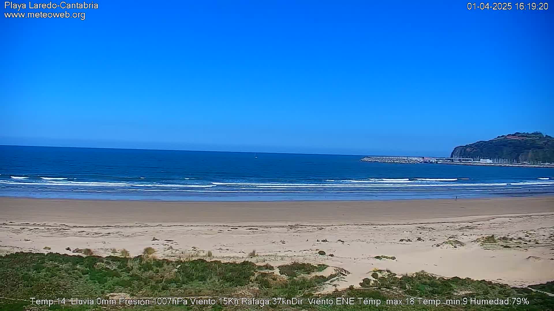 A wide sandy beach stretches towards a calm ocean under a clear blue sky.