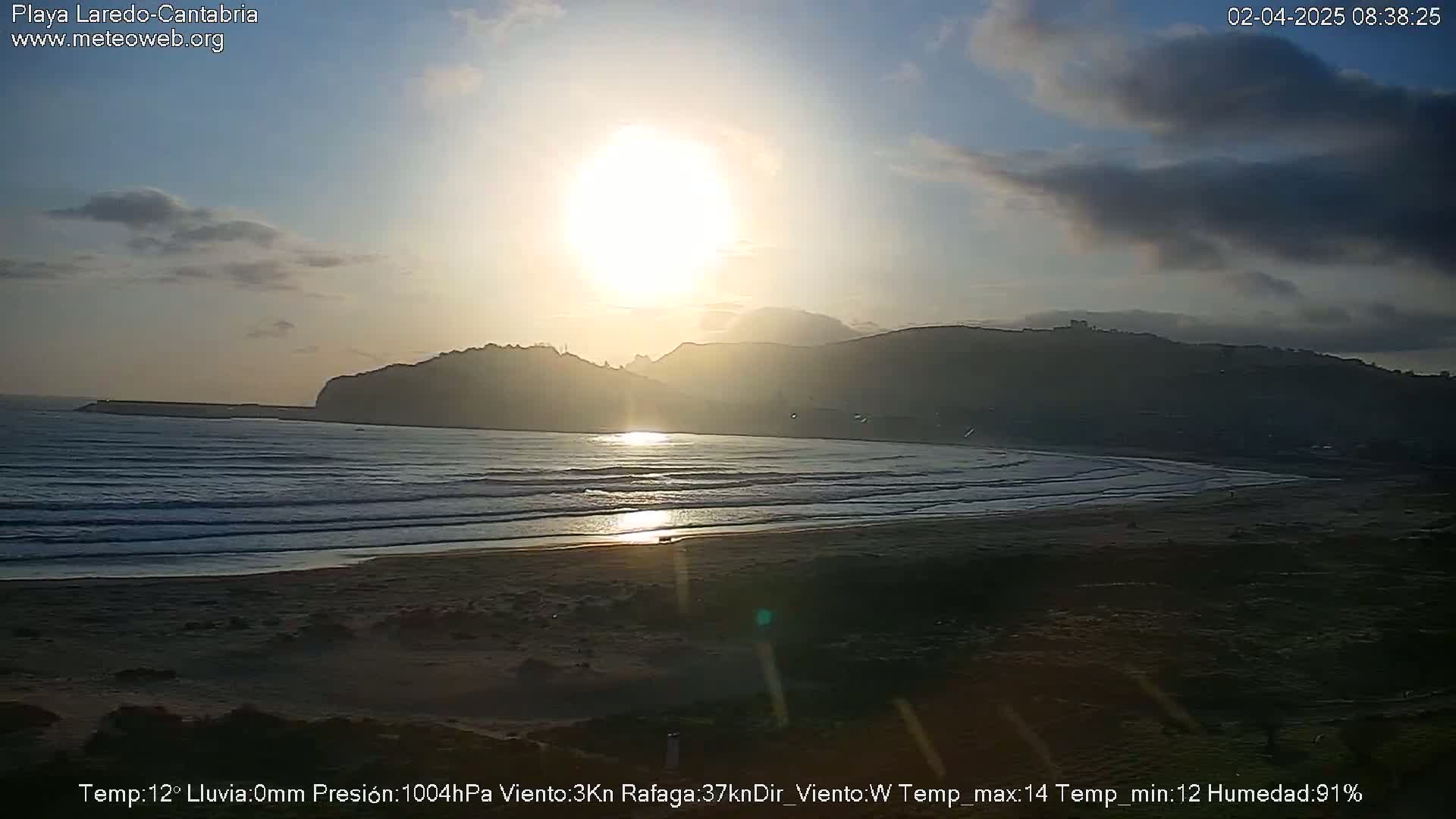 A beach with calm waves at sunset under a partly cloudy sky.