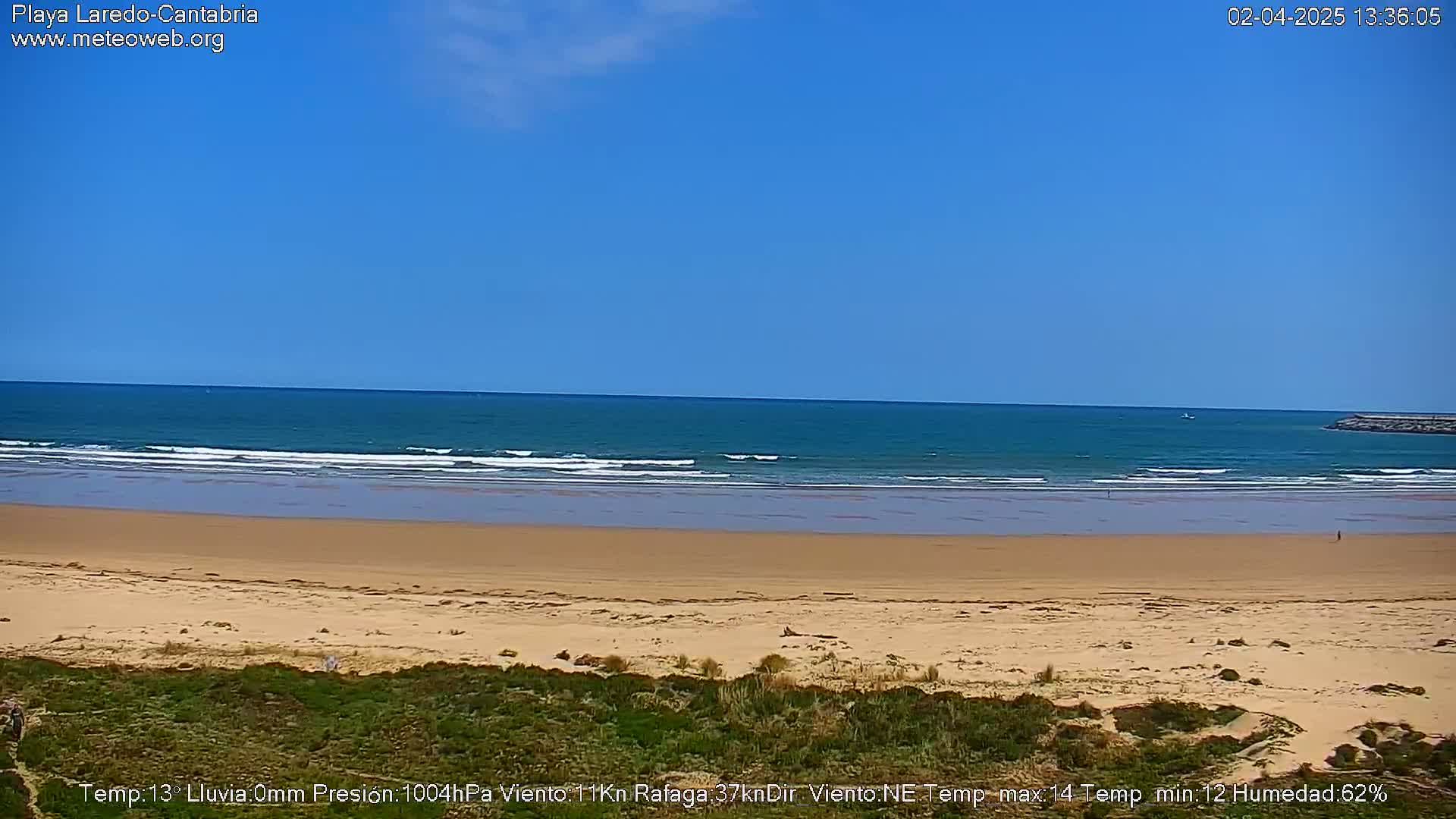 A sandy beach stretches to a calm, teal ocean under a clear blue sky.