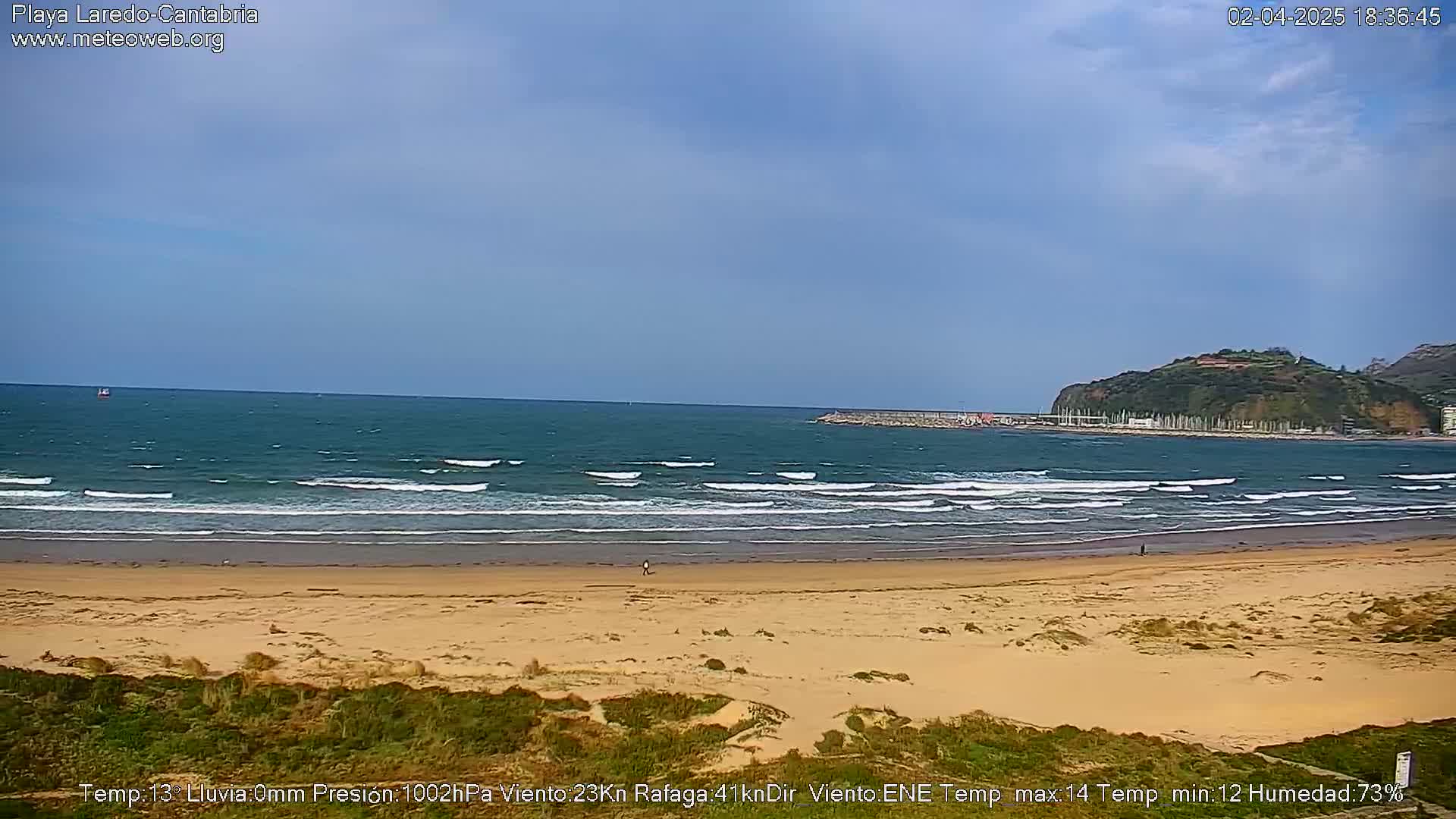 A sandy beach with small waves laps the shore under a partly cloudy sky.