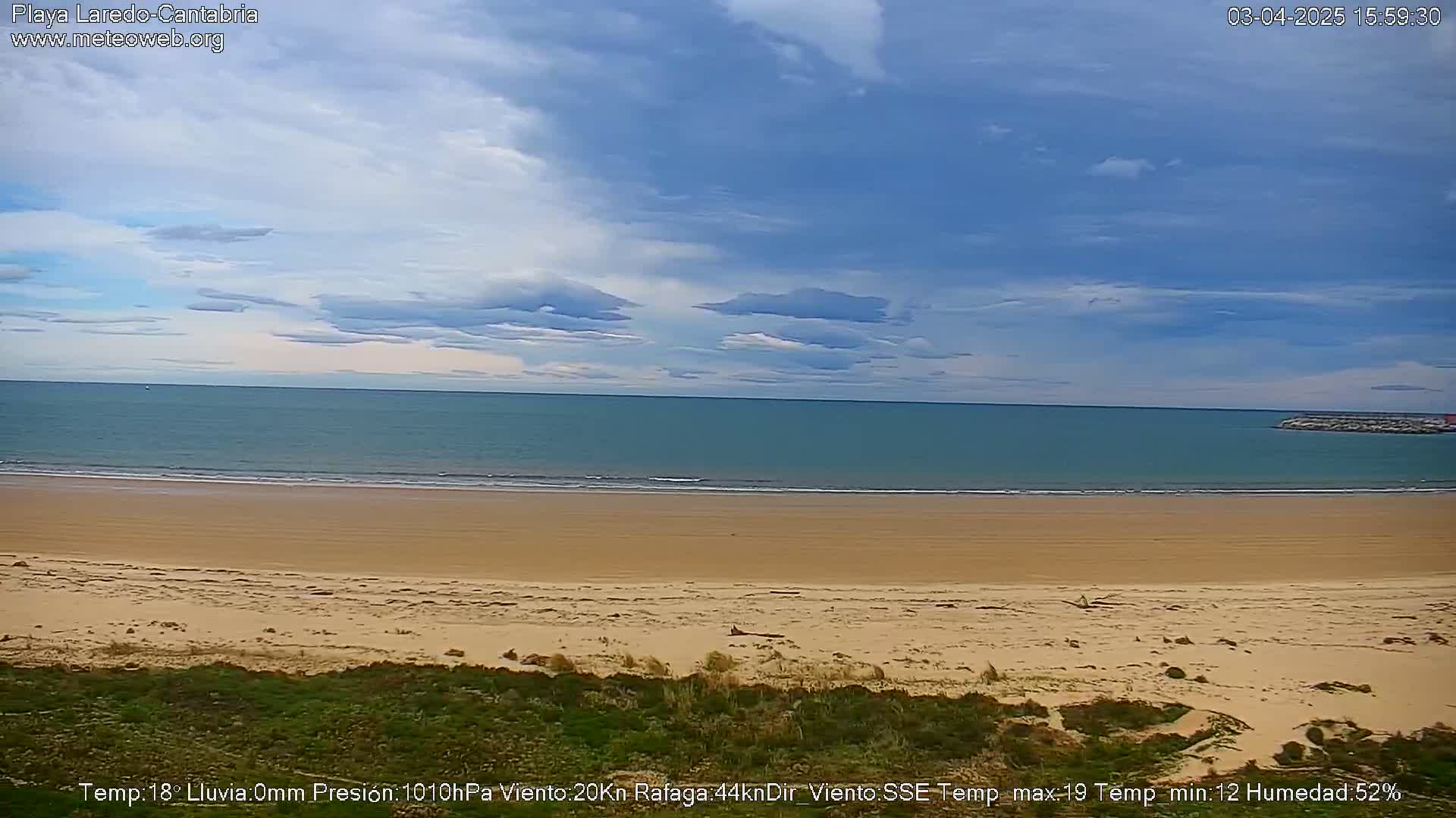 A sandy beach stretches to a calm, light-blue ocean under a partly cloudy sky.