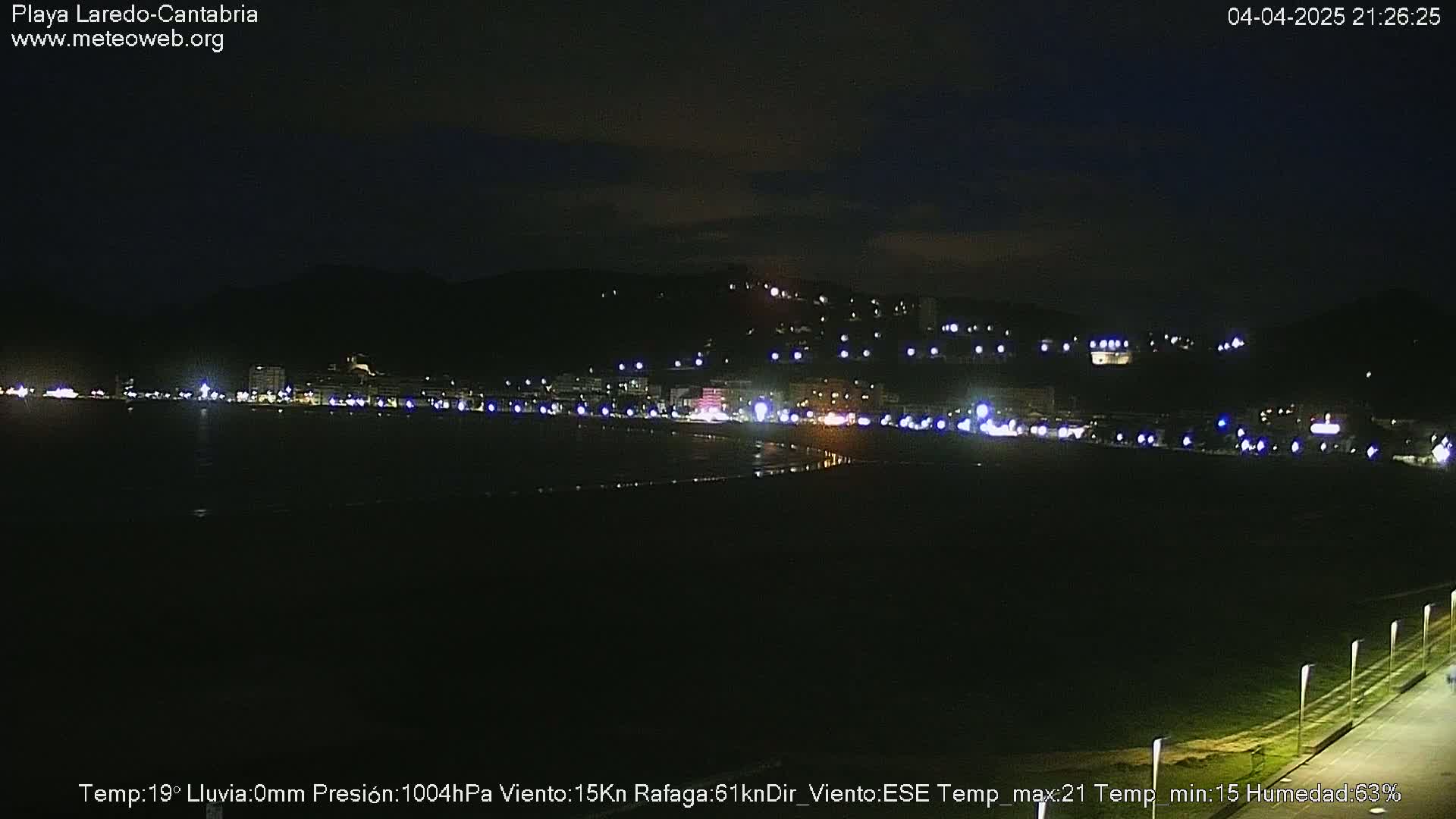 A nighttime view of a dimly lit beach town, situated against a dark hillside, under a clear night sky.