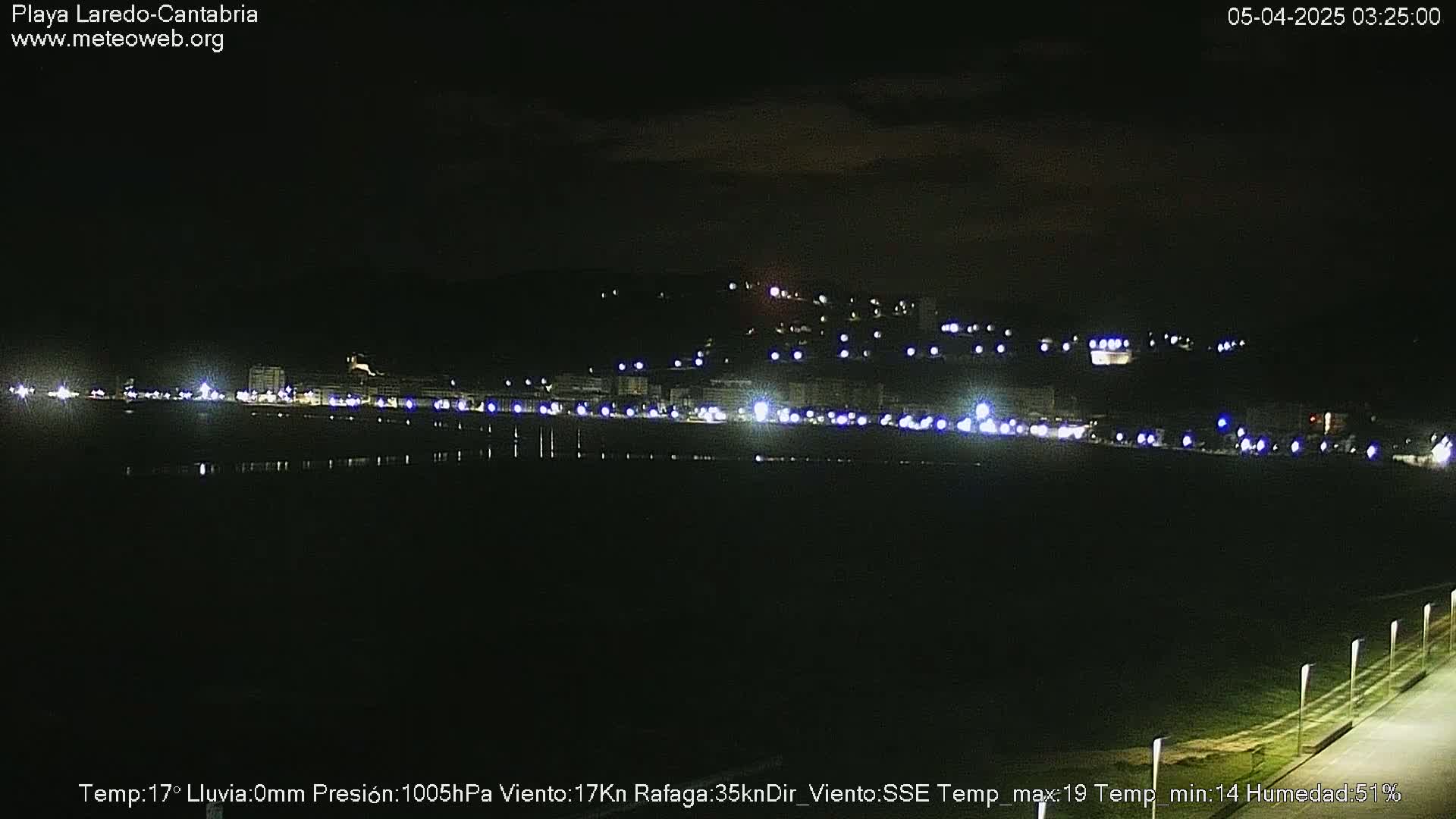 A nighttime view of a coastal town illuminated by lights, under a dark sky.