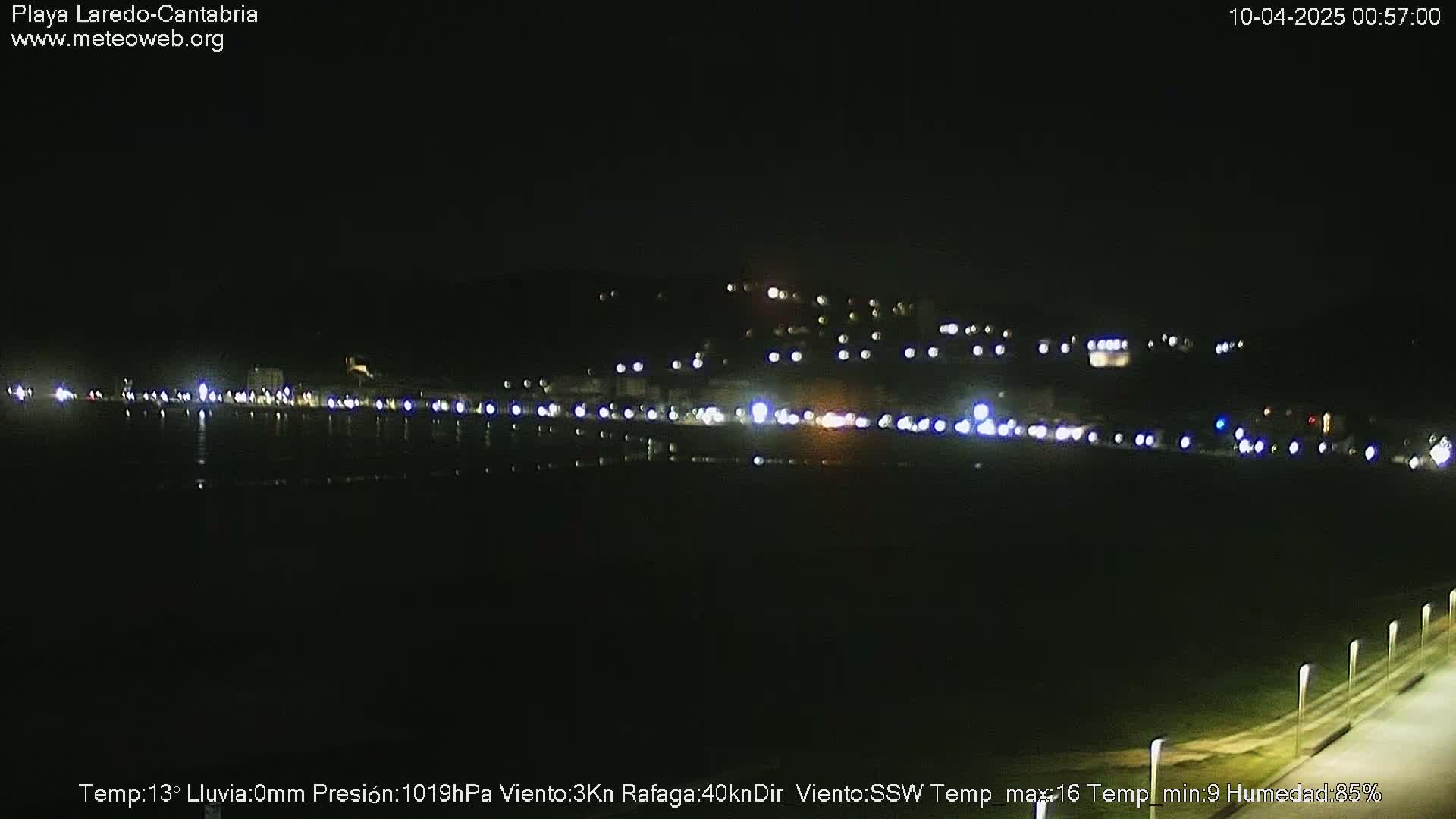 A nighttime view of a coastal town with lights reflecting on dark water under a clear sky.