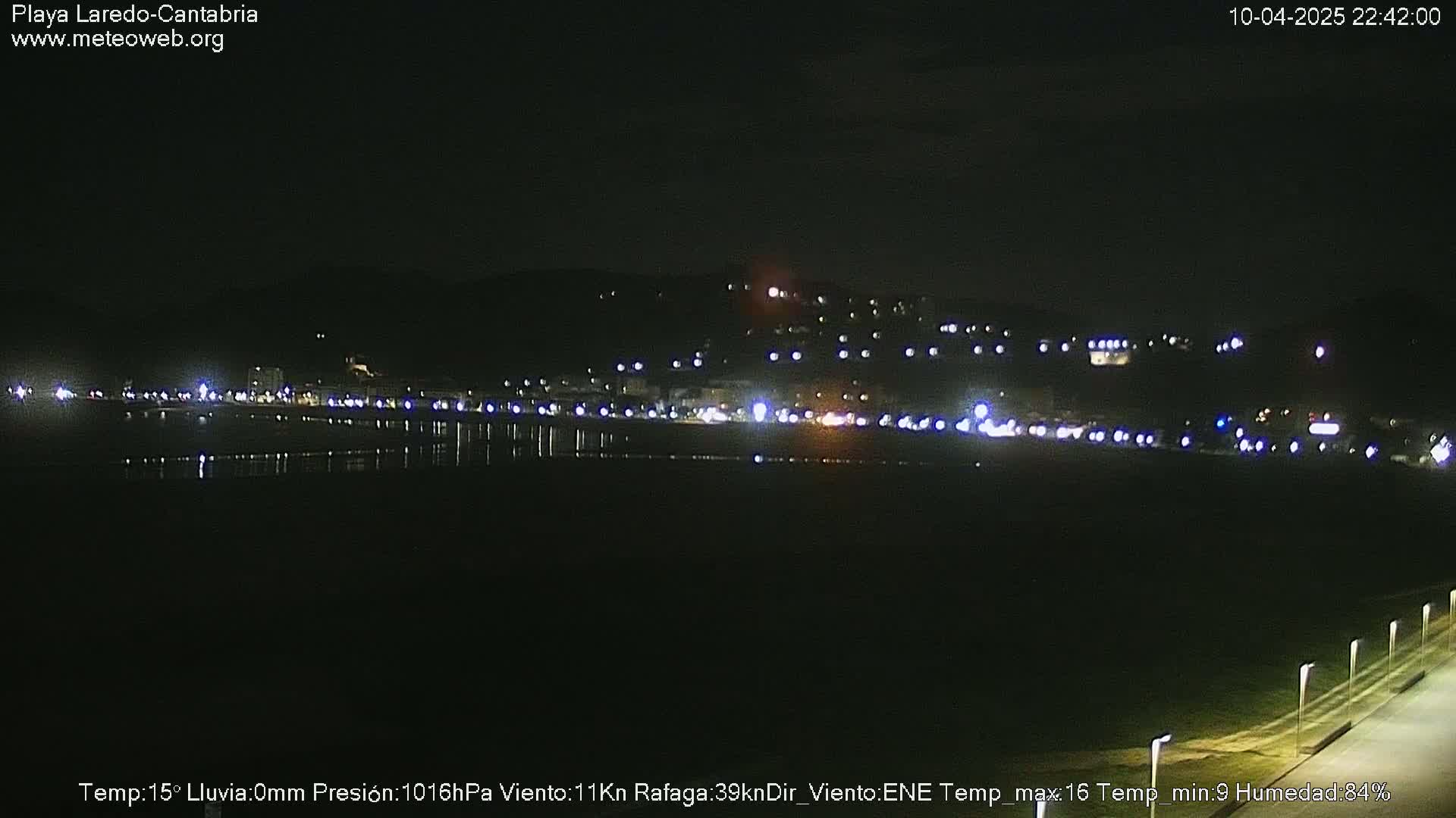 A nighttime view of a calm body of water reflecting the lights of a town situated on a hill in the background.
