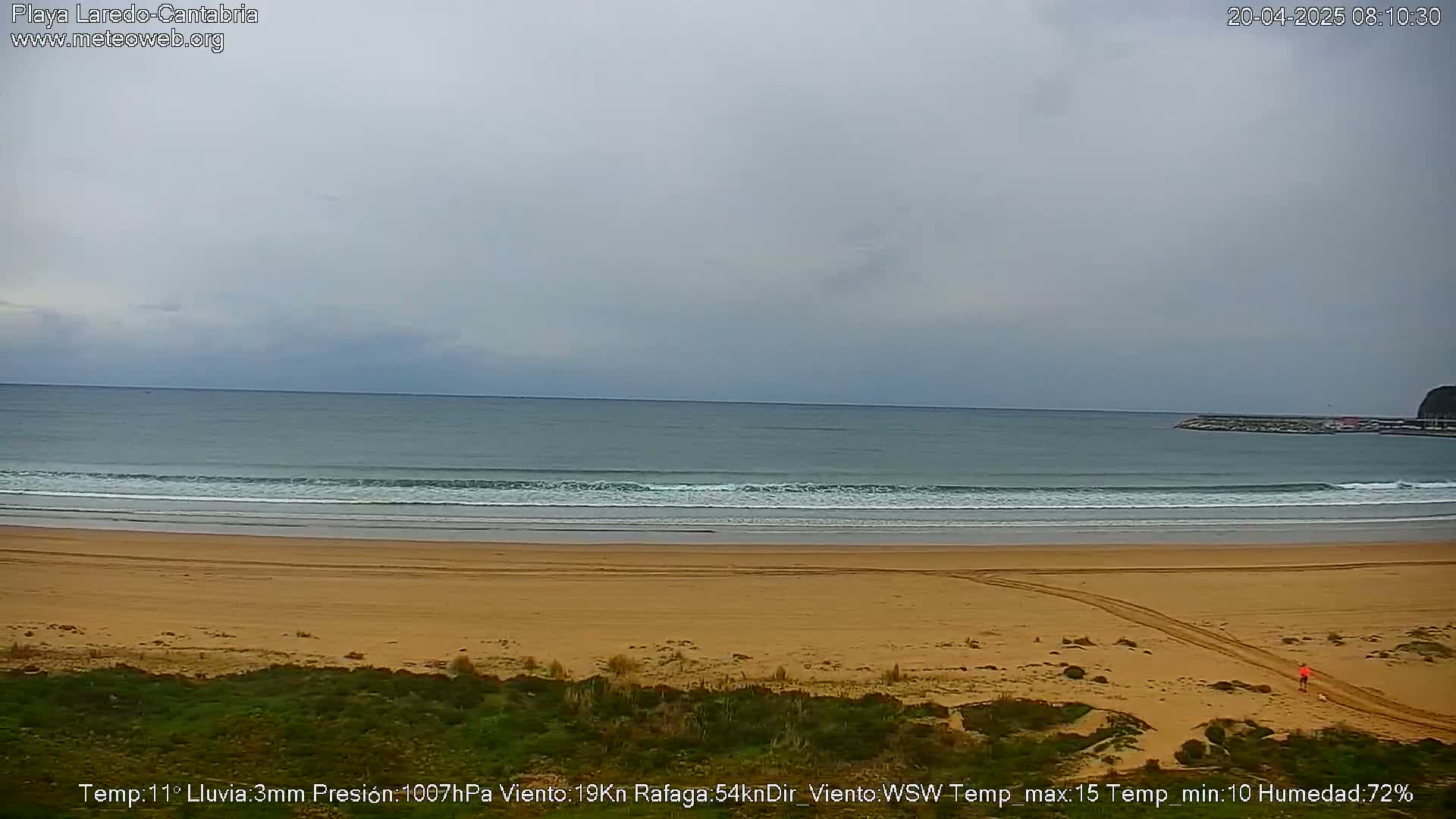 A wide sandy beach with gentle waves under an overcast sky.