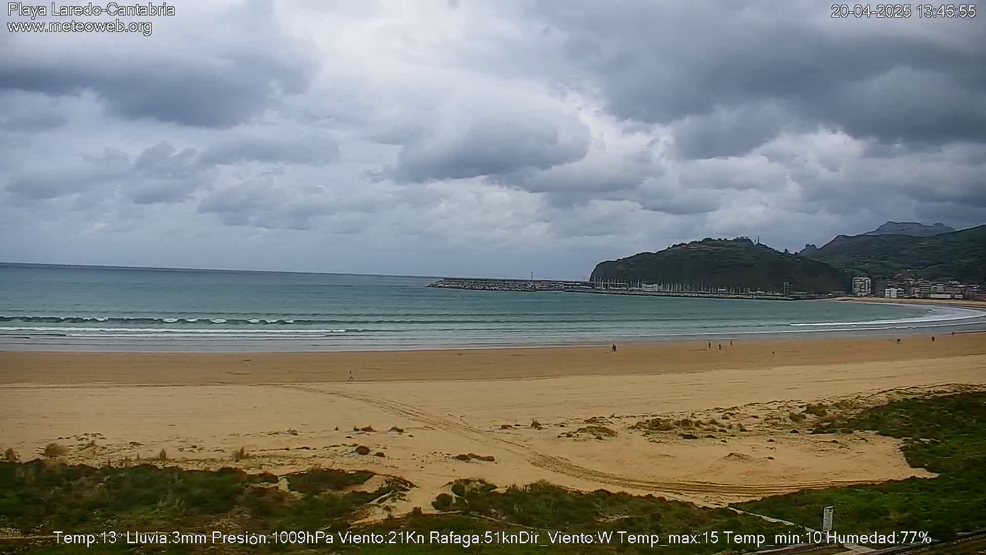 A sandy beach with gentle waves laps the shore under a cloudy sky.