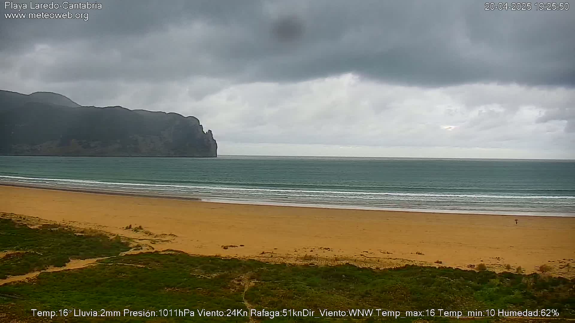 A sandy beach stretches to a calm ocean under an overcast sky, with a dark mountain visible in the distance.