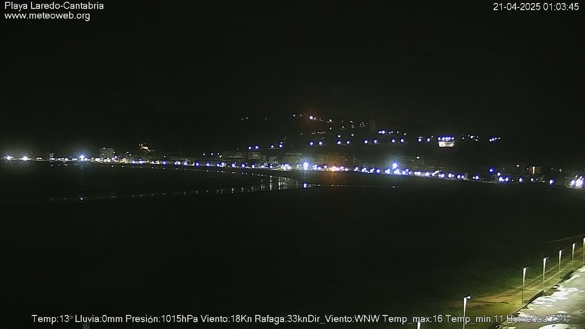 A nighttime view of a coastal town with faint lights, under a dark sky with no precipitation.
