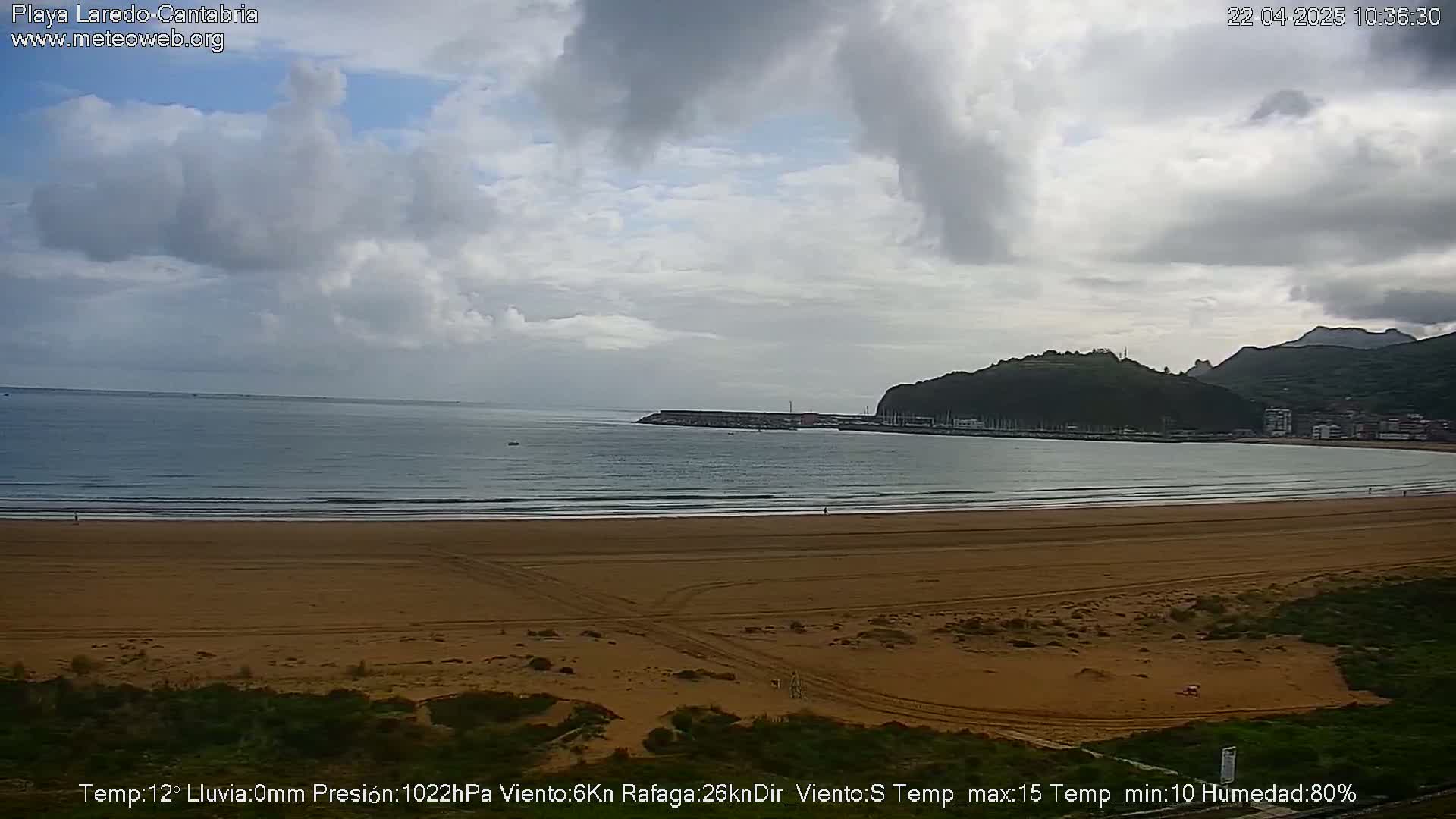 A wide sandy beach stretches to a calm ocean under a mostly cloudy sky.