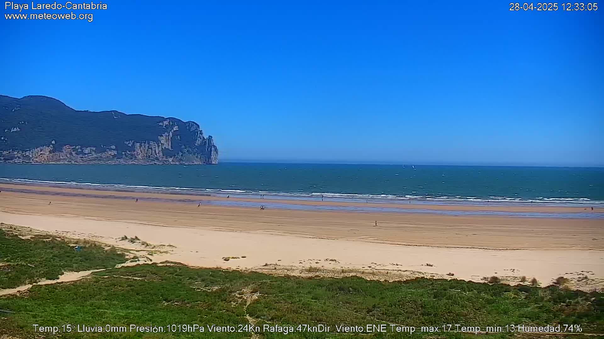 A sandy beach stretches out to a calm ocean under a clear blue sky, with a large, dark green landmass visible in the distance.