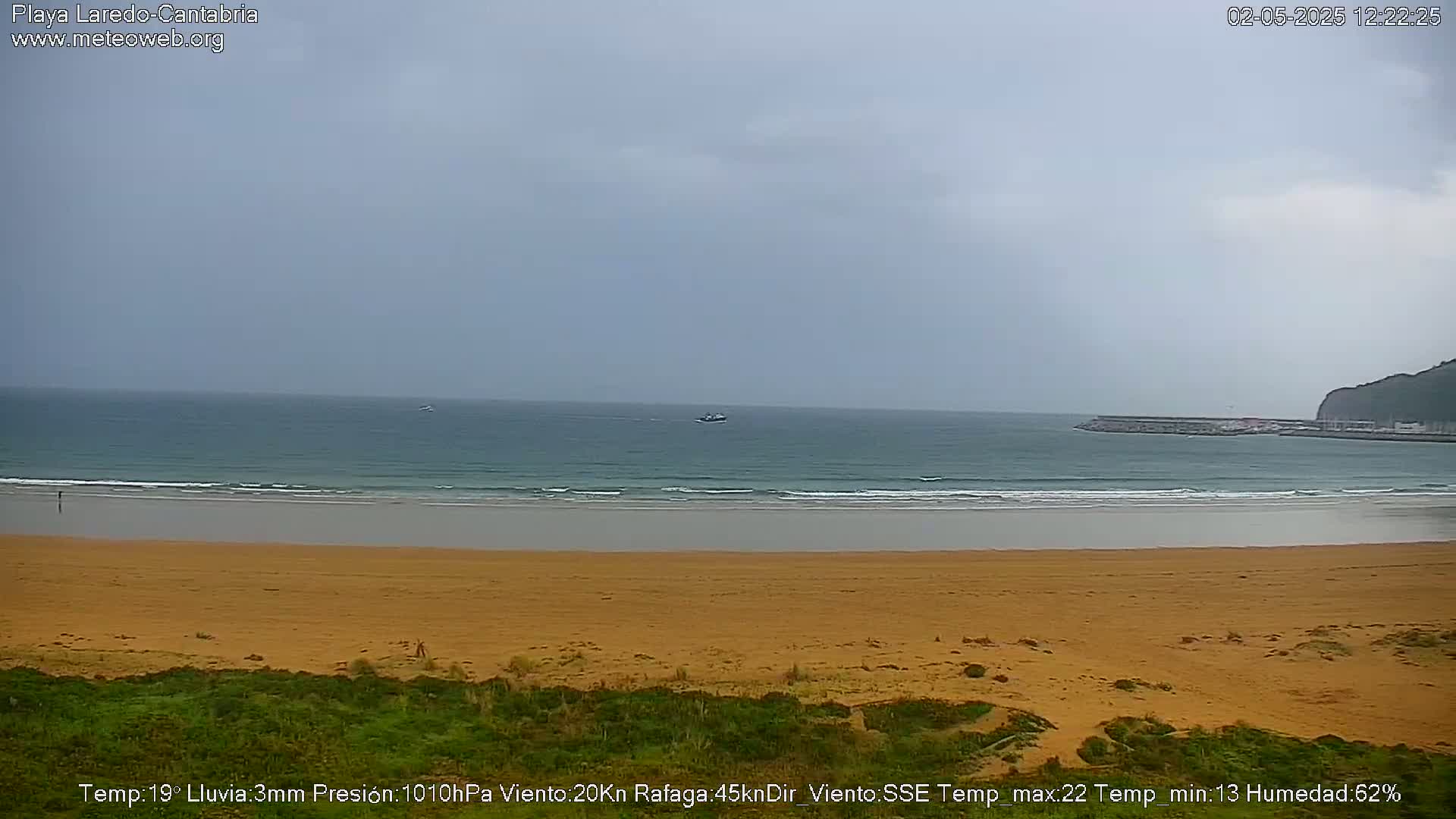 A sandy beach stretches to a calm ocean under an overcast sky.