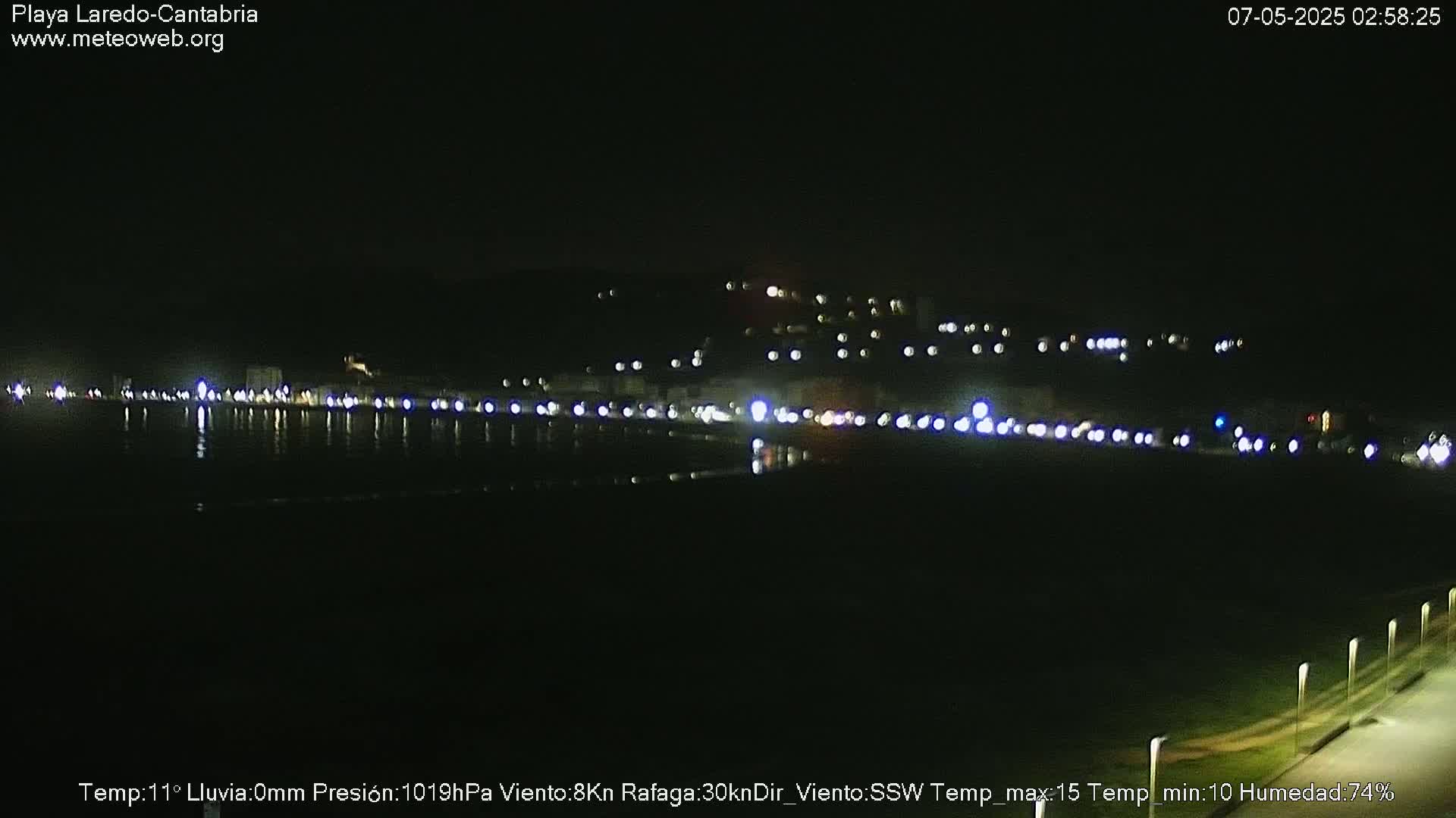 A nighttime view of a dark coastline with faintly visible lights from buildings and vehicles on the shore.
